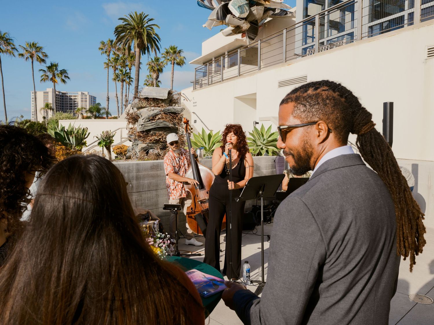 Live band performing at an outdoor rooftop event with palm trees and modern architecture in a sunny coastal setting.