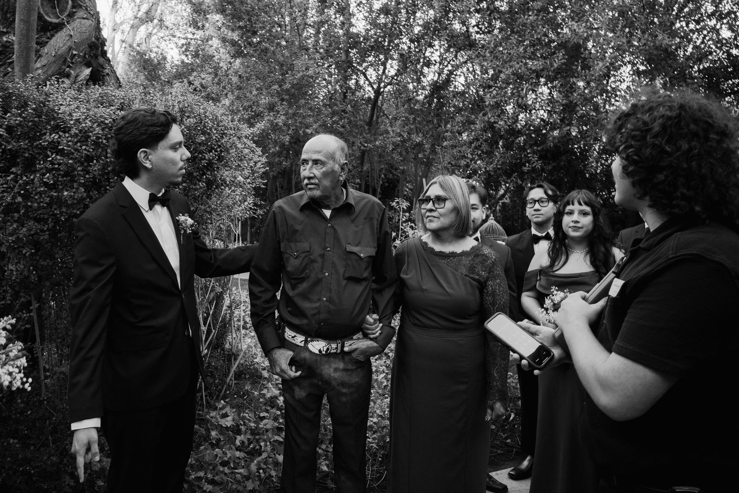 Black and white photo of groom conversing with guests at outdoor wedding.