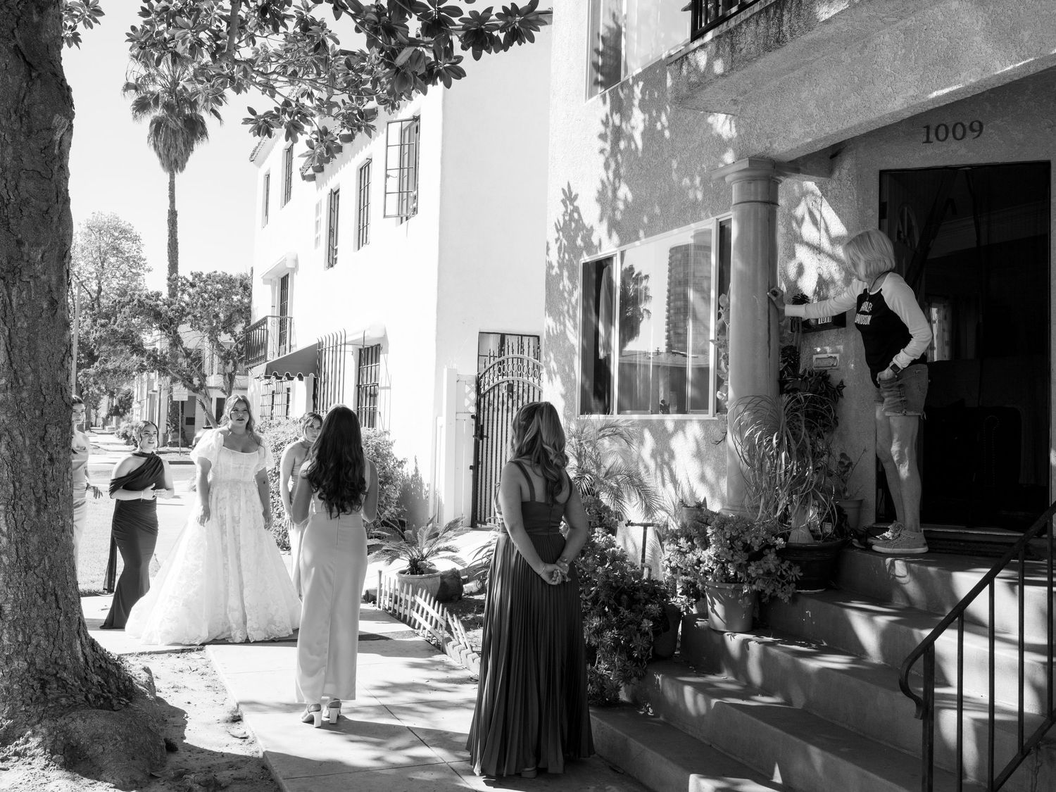 Black and white photo of bride and bridesmaids gathered outside an apartment building on a sunny wedding day.