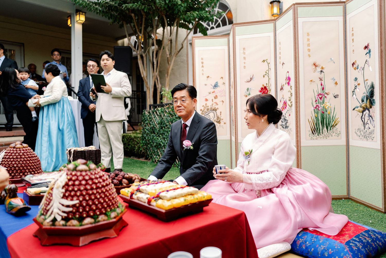 Traditional Korean wedding paebaek ceremony with family seated beside table of ceremonial foods.