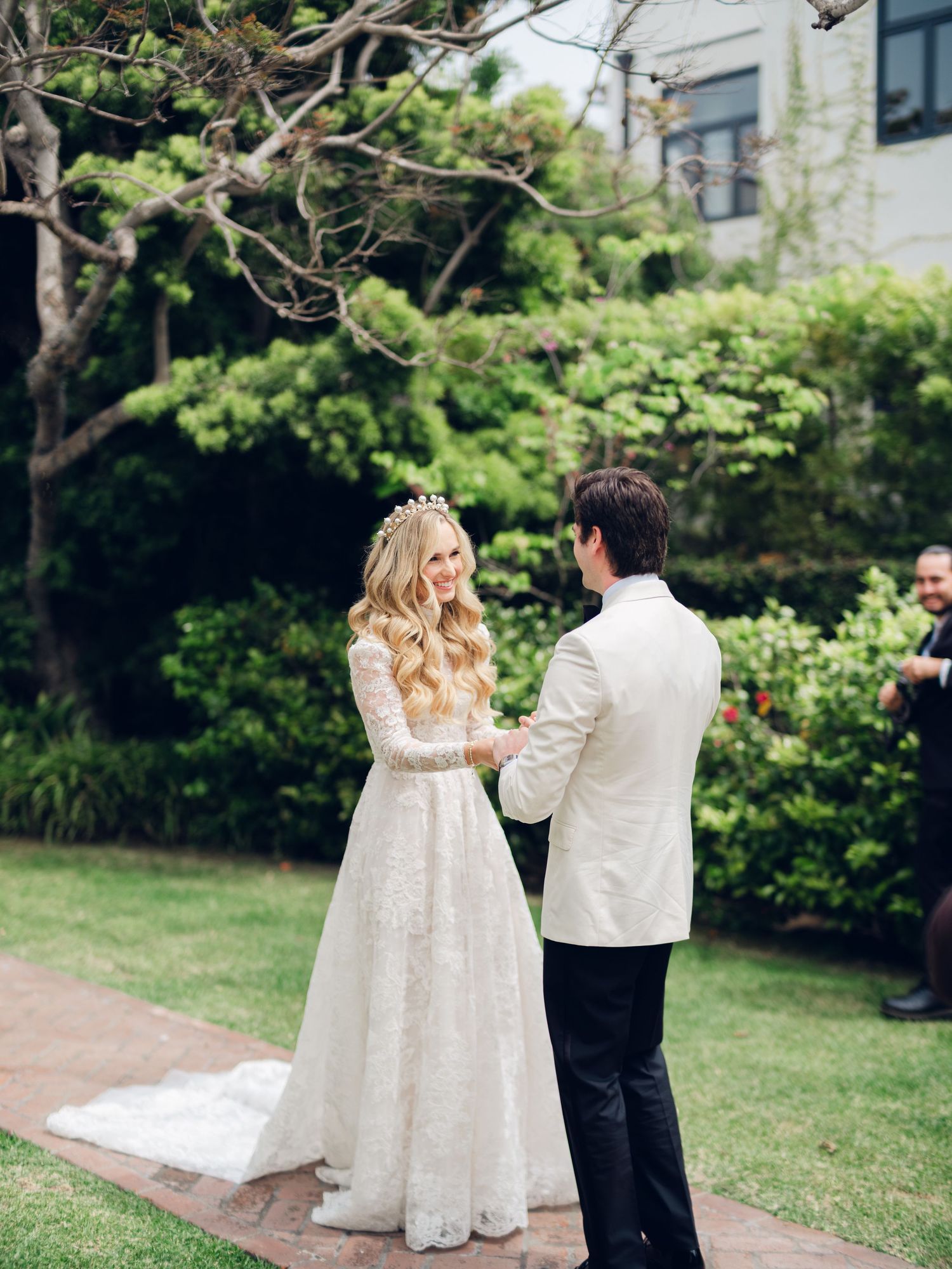 Bride and groom hold hands during outdoor garden wedding ceremony with lush green backdrop.