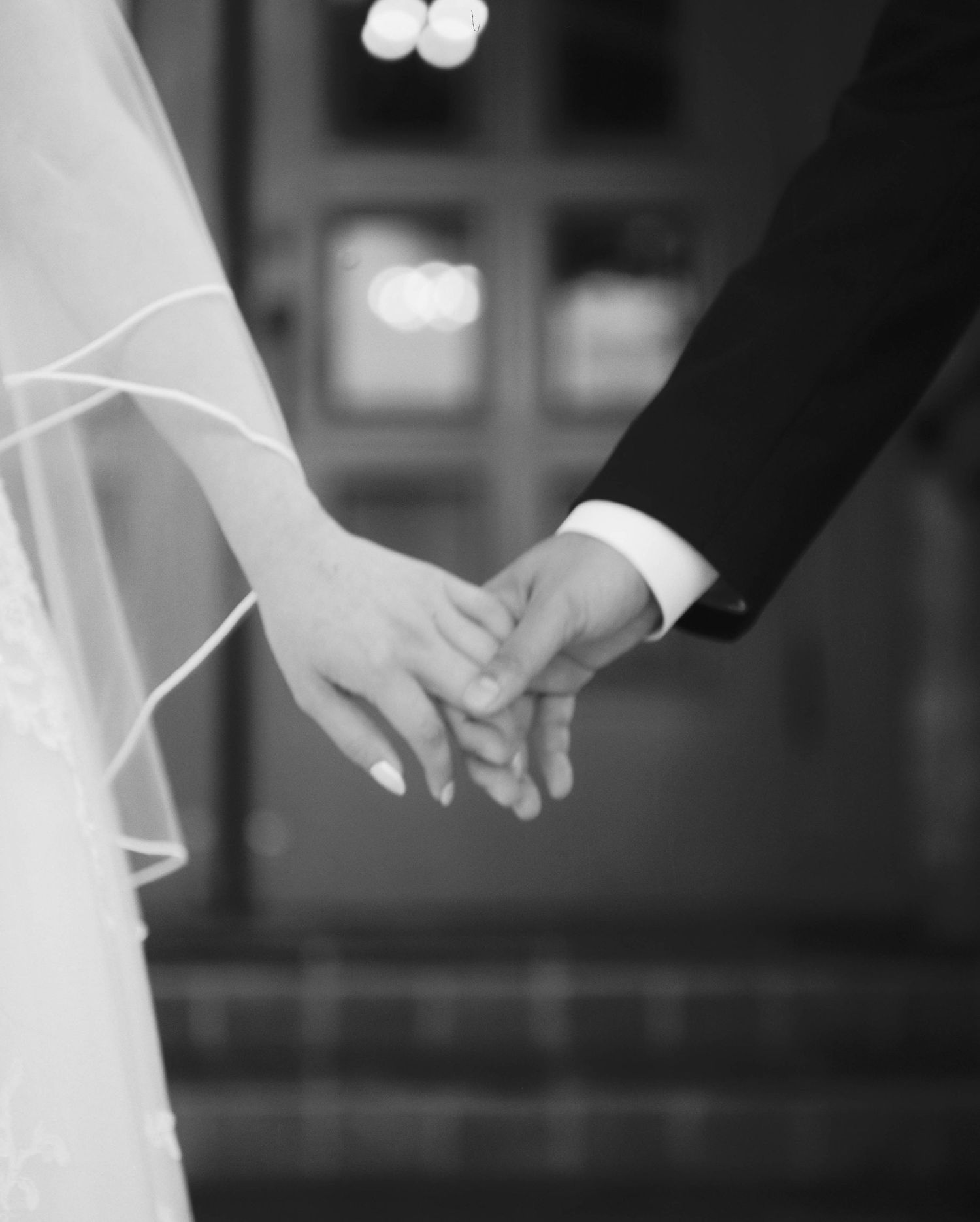 Black and white close-up of bride and groom holding hands at wedding ceremony.