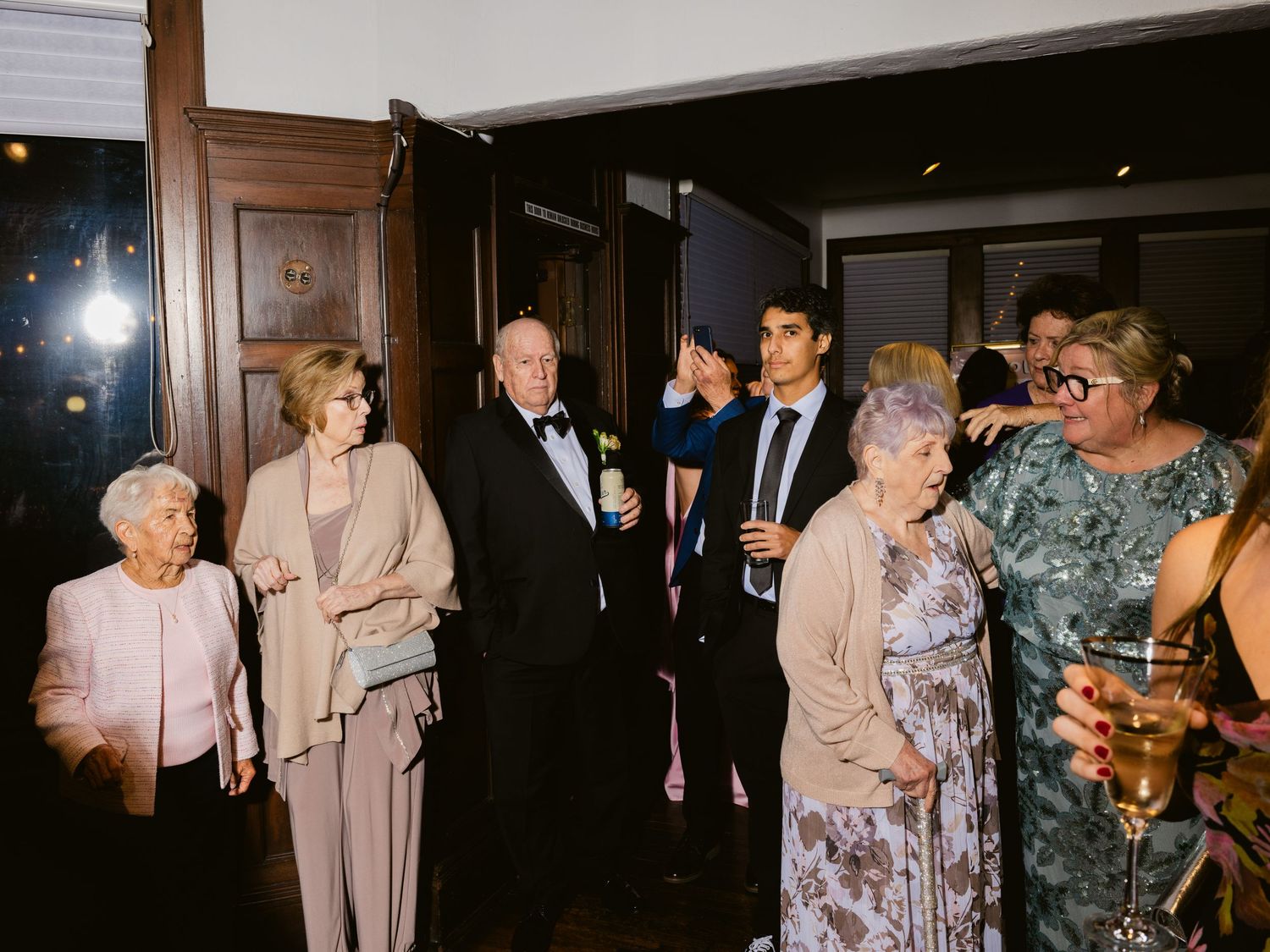 Wedding guests mingling indoors in formal attire during a reception at a wood-paneled venue.