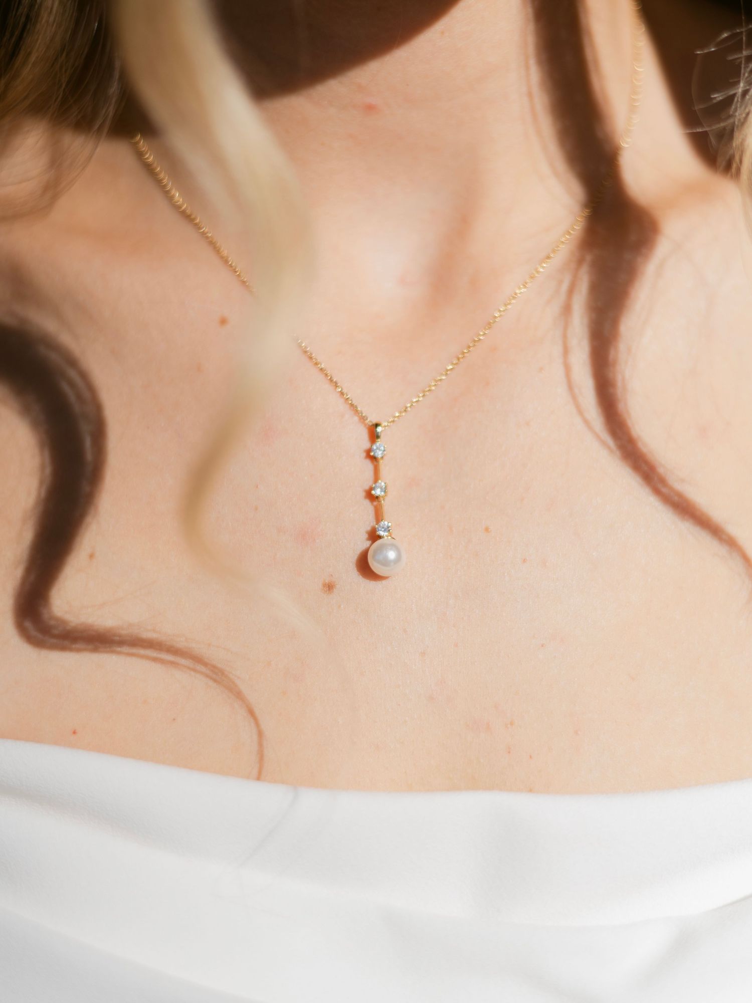 Close-up of delicate gold chain necklace with pearl pendant on bride in white dress.