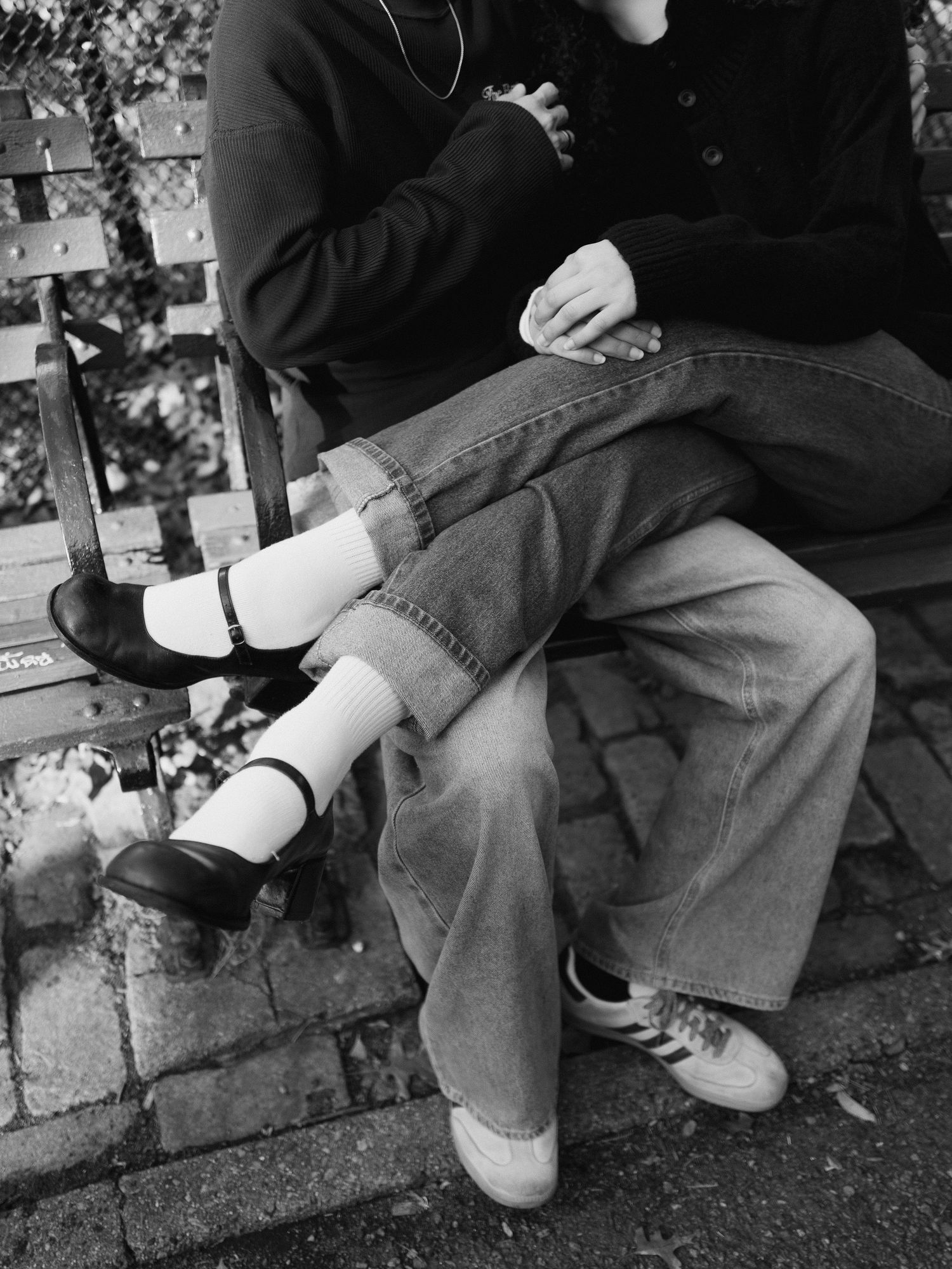 Close-up black and white photo of a couple sitting together on a park bench, legs intertwined.