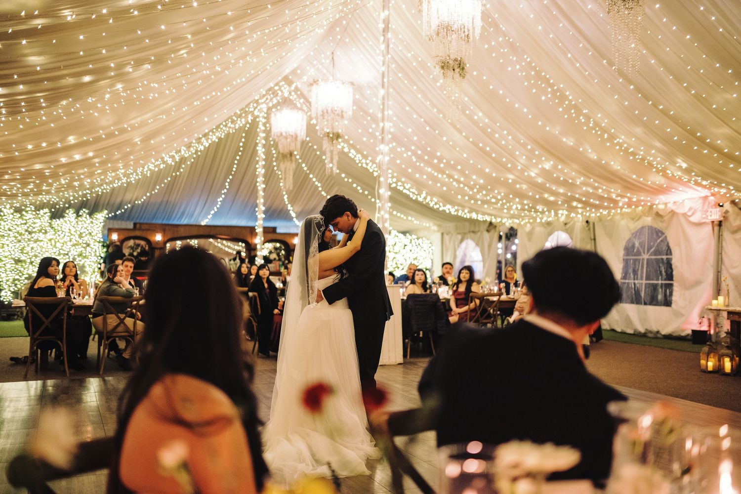 Couple shares first dance under stunning canopy of warm fairy lights at elegant wedding reception.