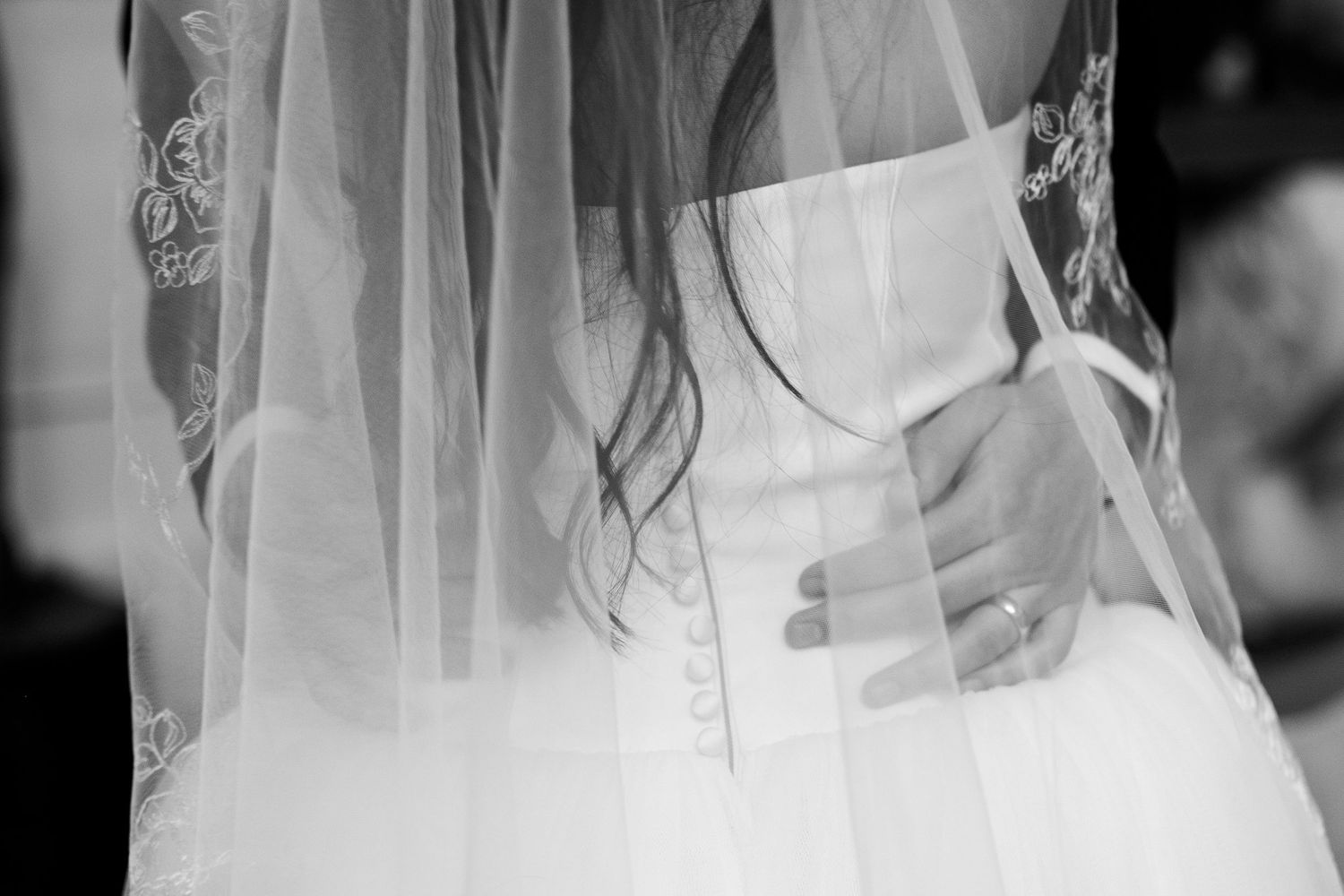 Close-up black and white photo of bride in wedding gown with flowing veil and lace details.