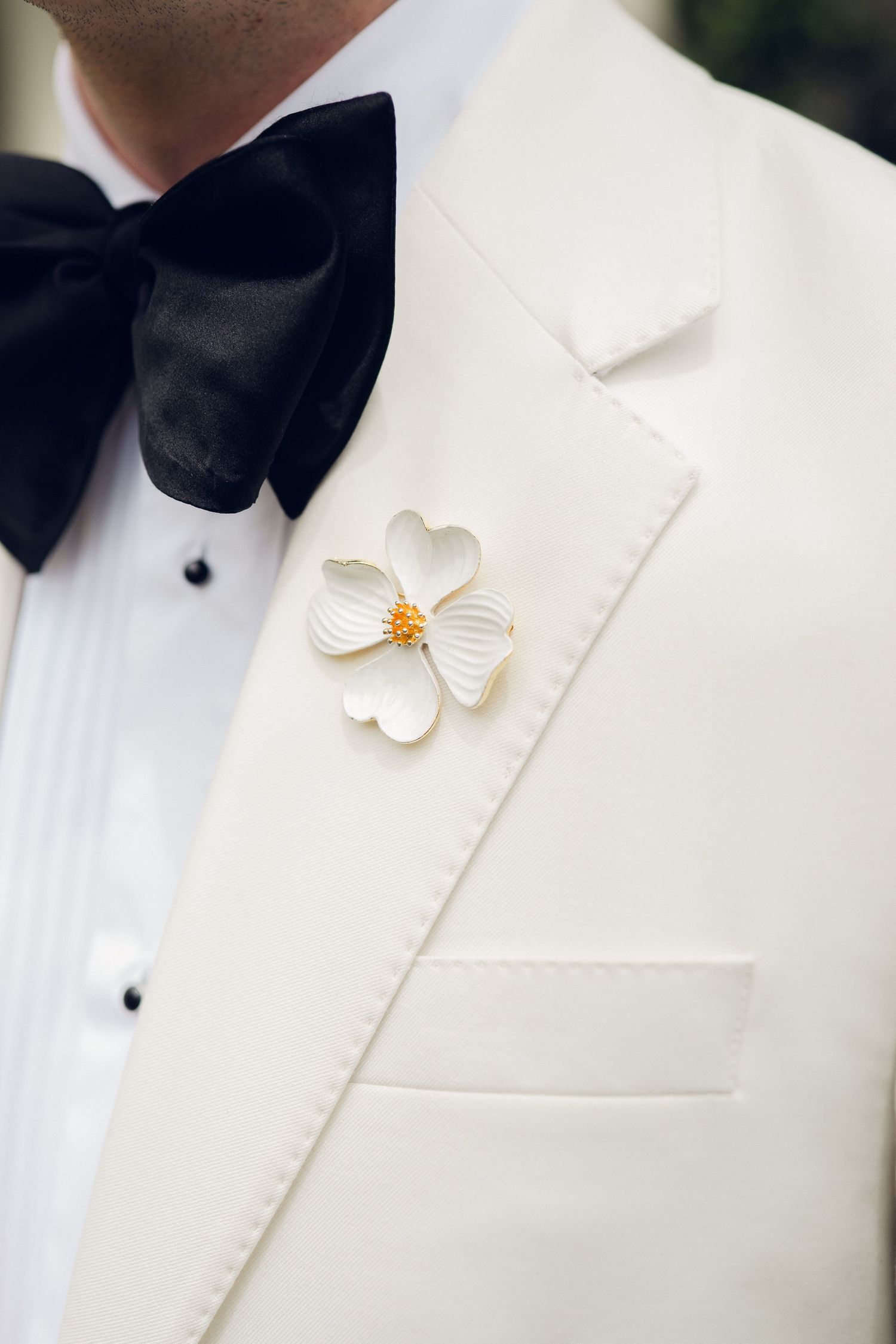 Groom in white tuxedo jacket with black bow tie and white floral boutonniere close-up detail.