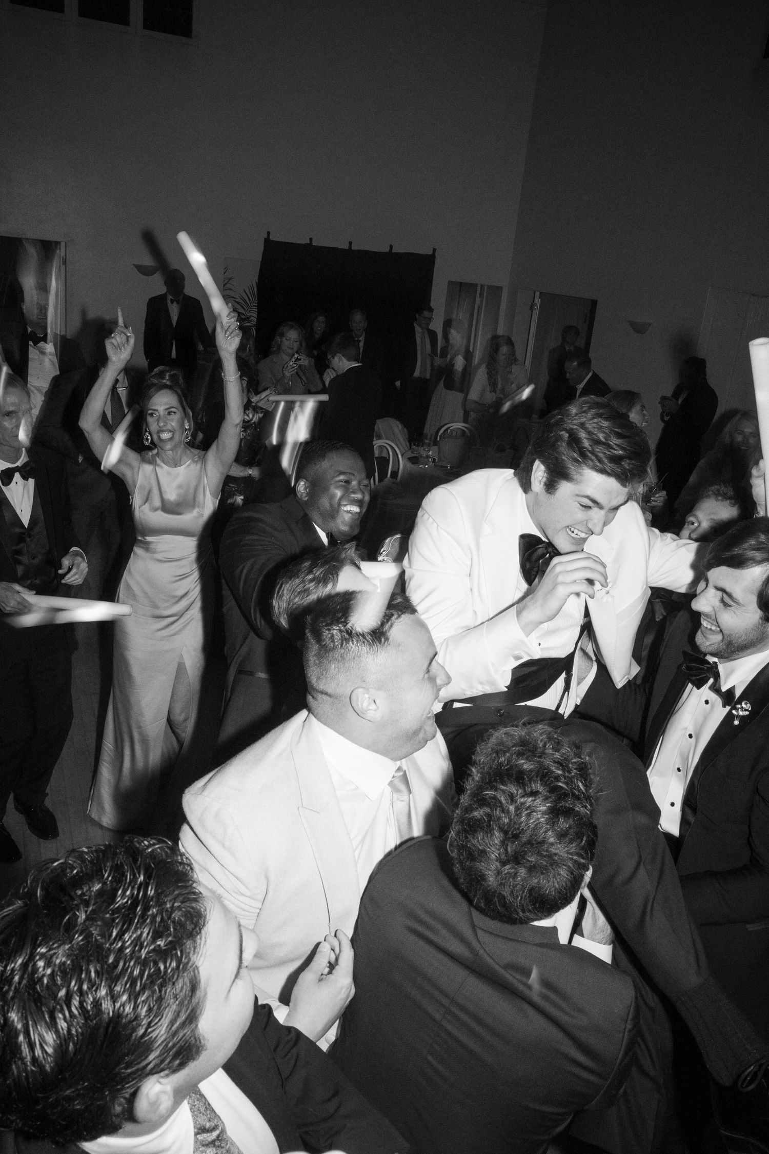 Black and white photo of wedding guests energetically celebrating on the dance floor at a reception.