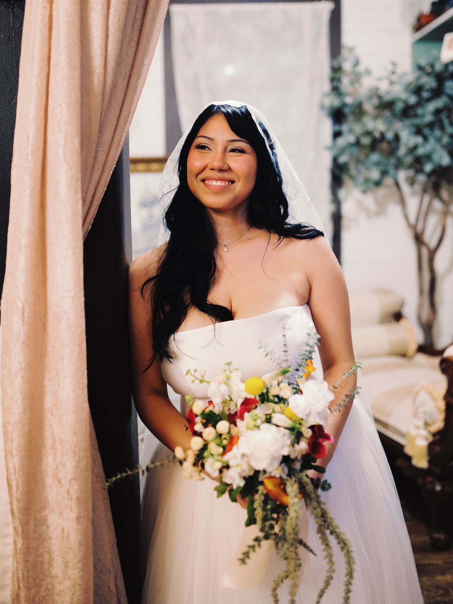 Radiant bride in strapless white gown holds a colorful cascading bouquet at her wedding venue.