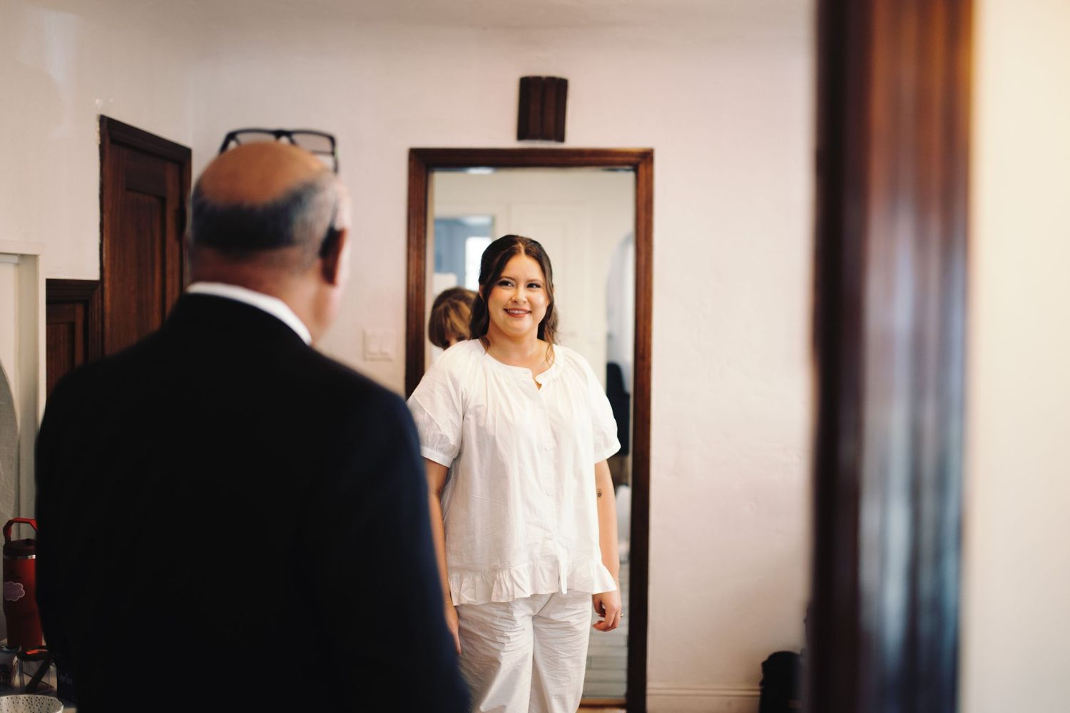 Smiling bride in white outfit shares a tender moment with a guest in a warmly lit room.
