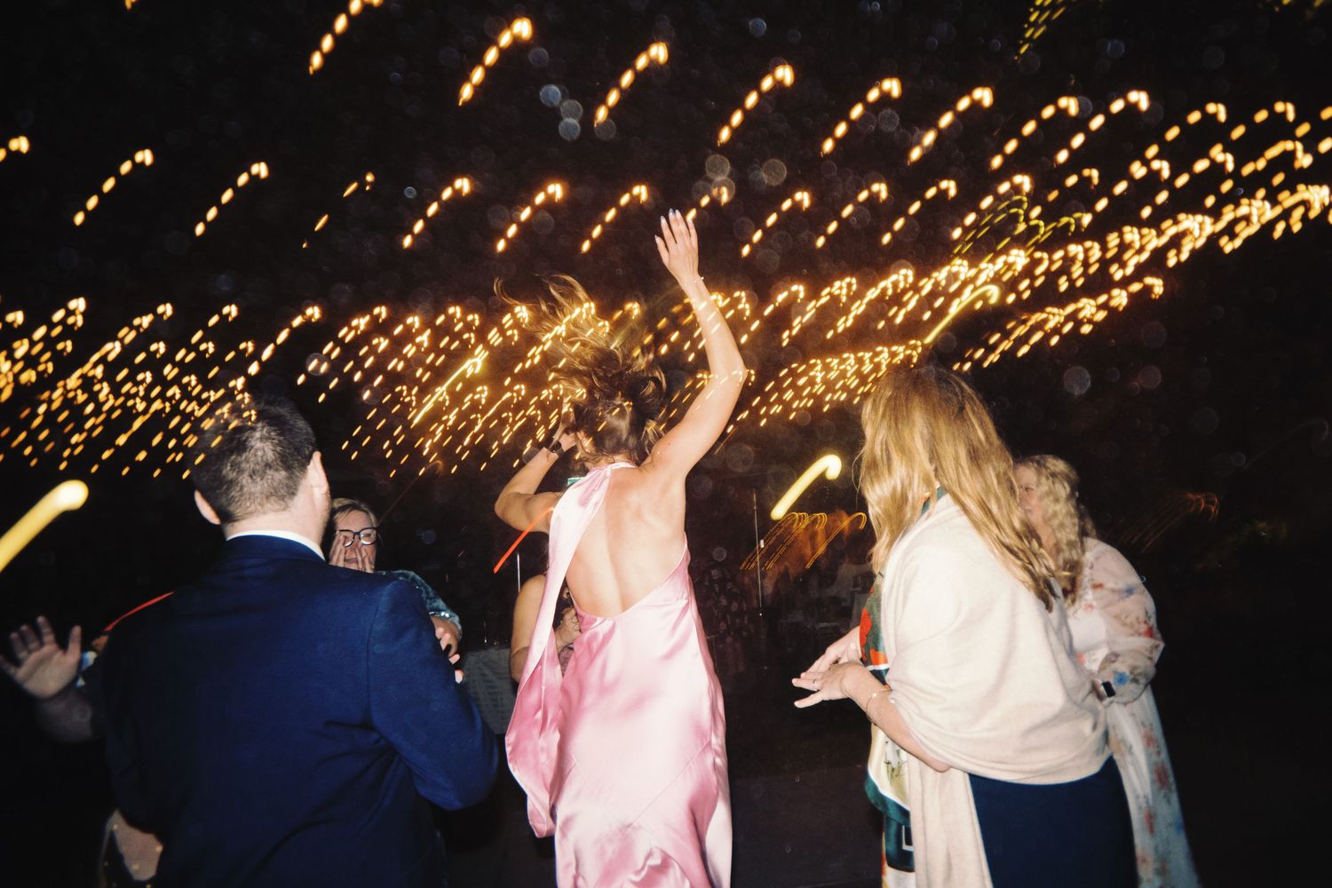 Wedding guests dancing outdoors at night under a canopy of sparkling string lights.