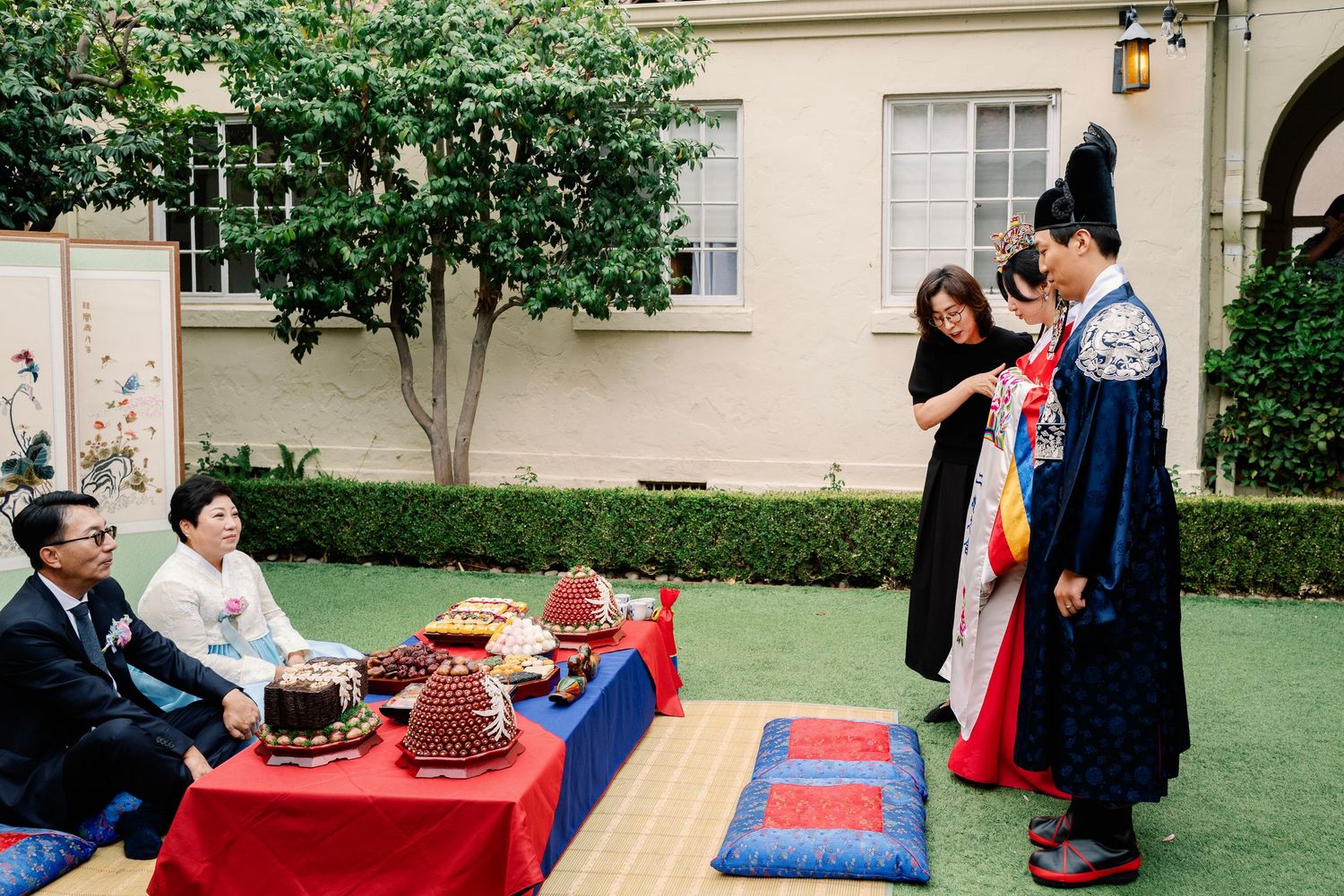 Traditional Korean paebaek ceremony with couple in hanbok bowing before seated family members.