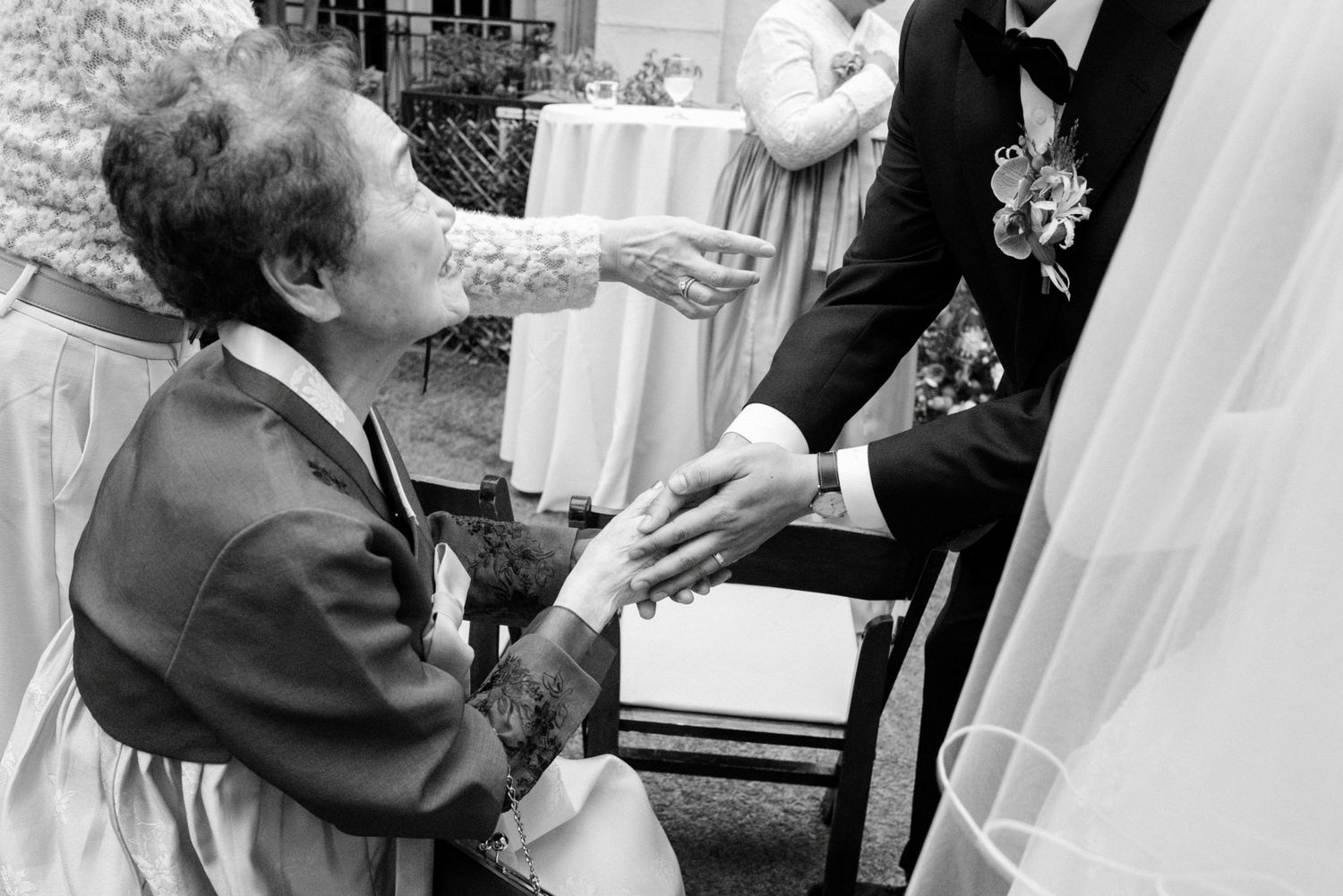 Emotional elderly guest holds groom's hand in touching black and white wedding candid moment.