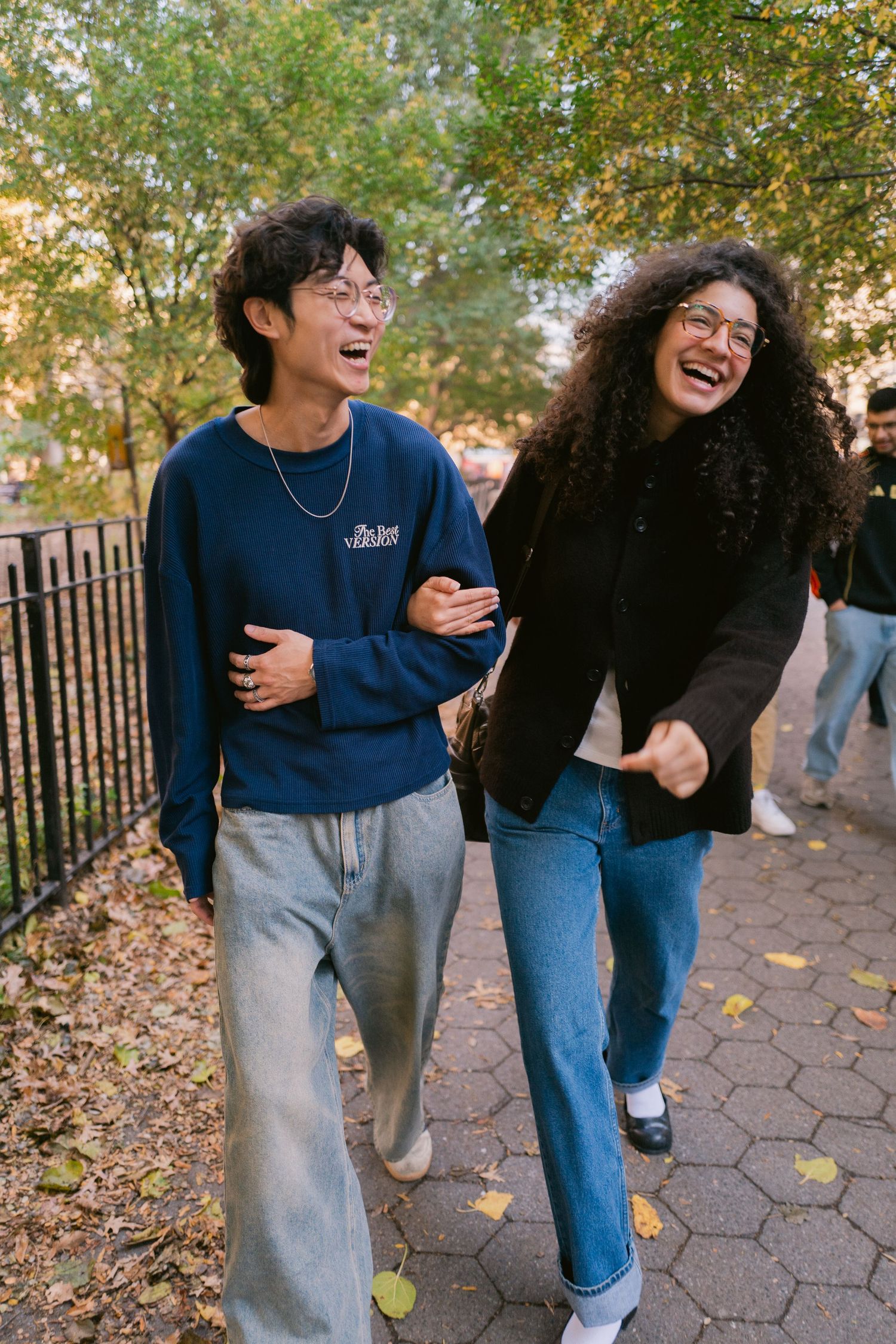 Happy couple laughing and walking together along a tree-lined park path on a sunny day.
