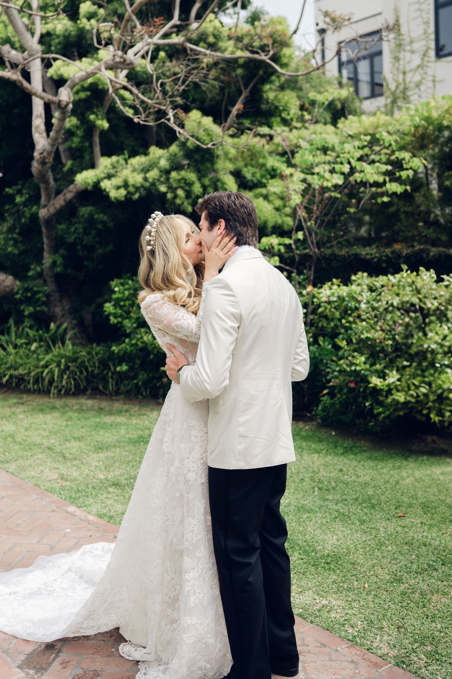 Bride and groom share first kiss during outdoor wedding ceremony surrounded by lush greenery.