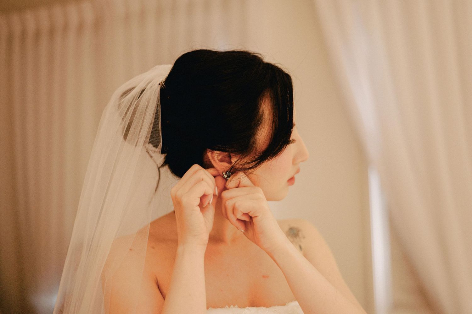 Bride with dark hair and veil fastening her earring before the wedding ceremony.