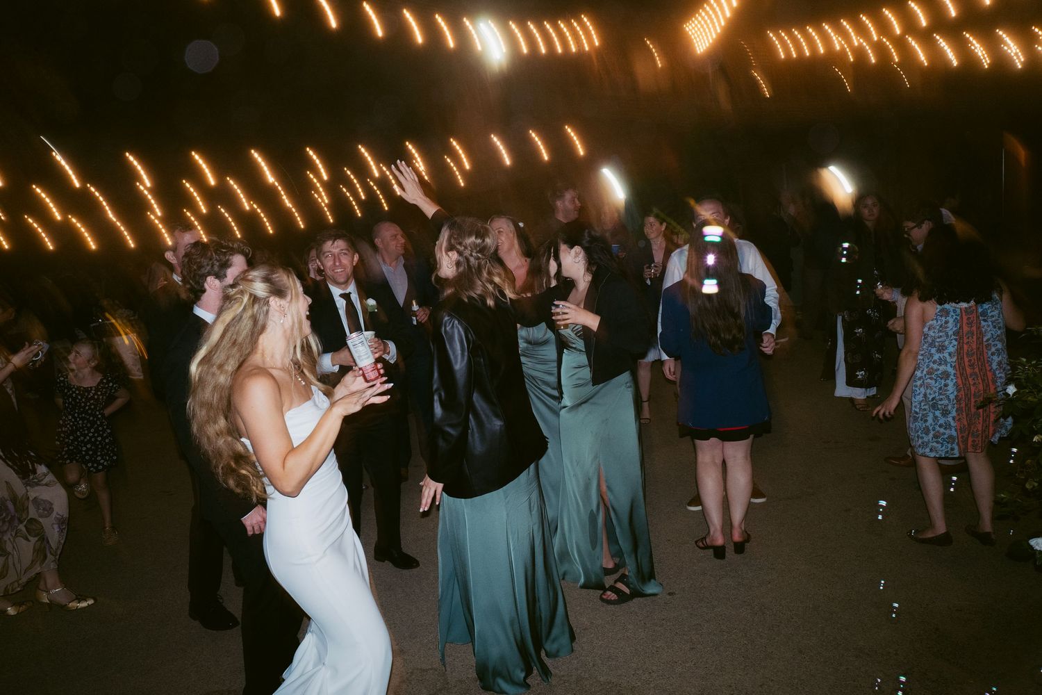 Wedding guests dancing under string lights at an outdoor evening reception.
