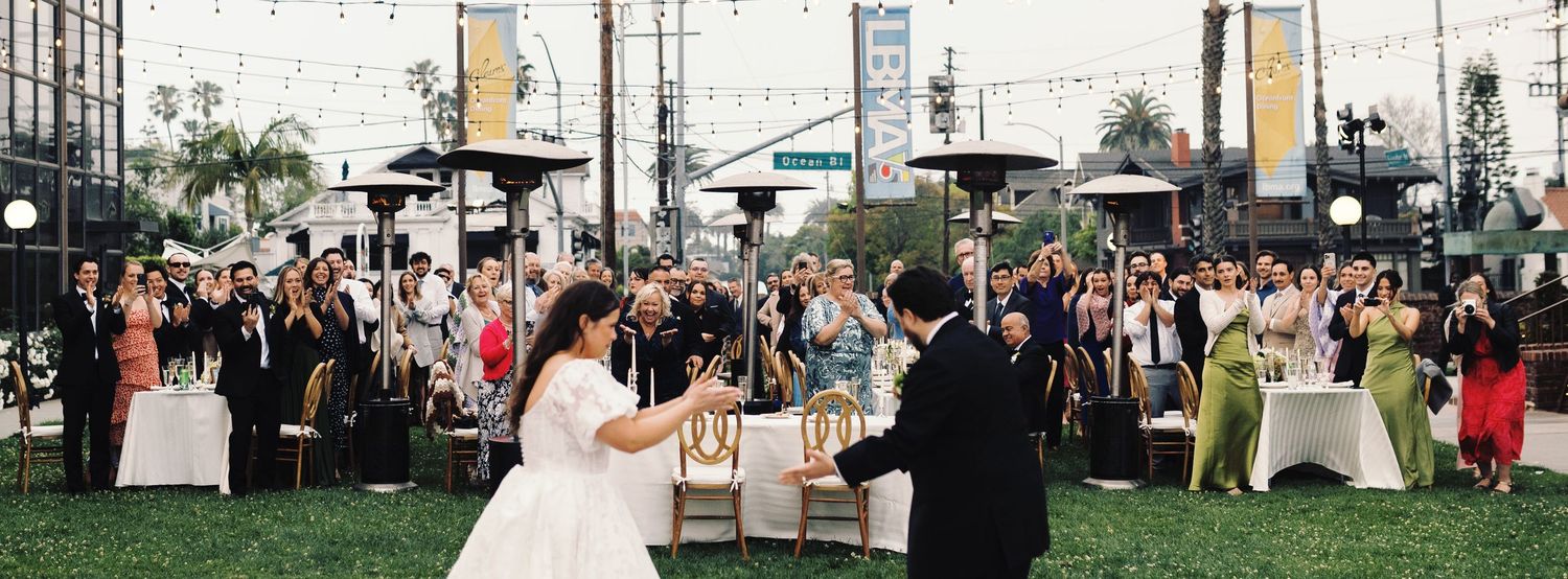 Bride and groom share a romantic moment seated together during outdoor wedding reception with guests.