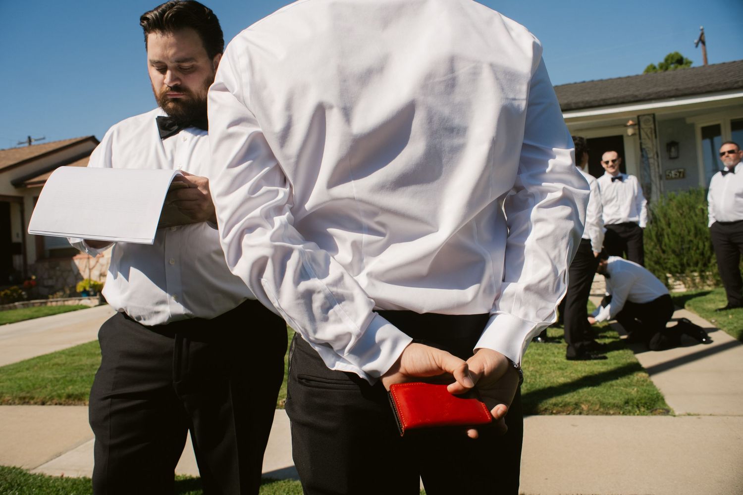 Groomsmen in white shirts and bow ties preparing outside before wedding ceremony.