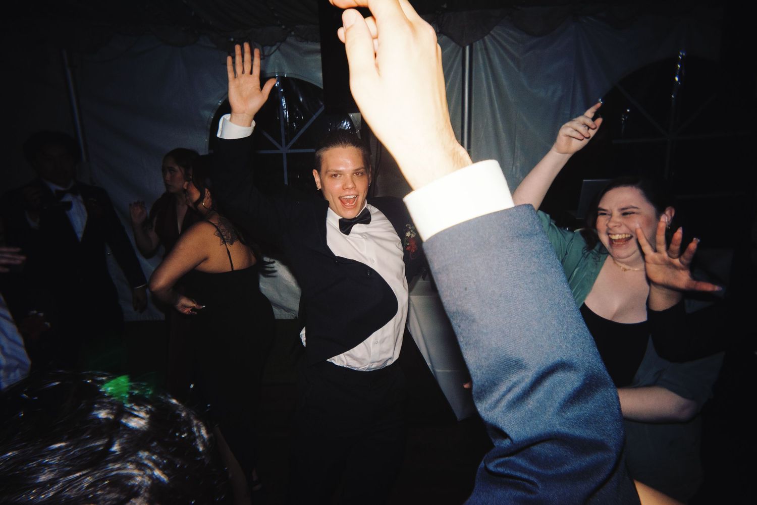 Guests dancing and celebrating with hands raised at energetic wedding reception party.