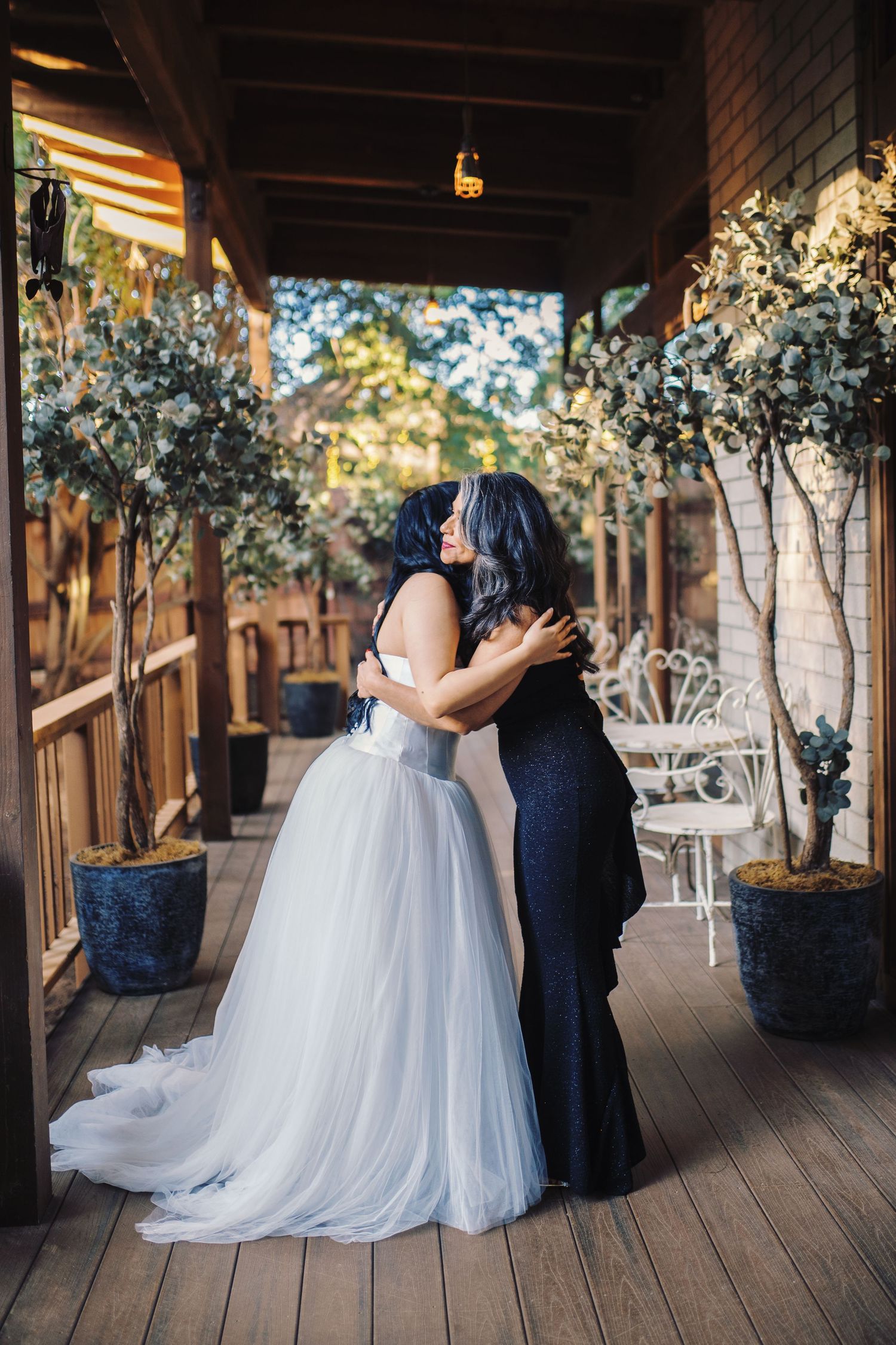 Bride in white tulle gown shares a heartfelt embrace with her mother in a navy dress outdoors.