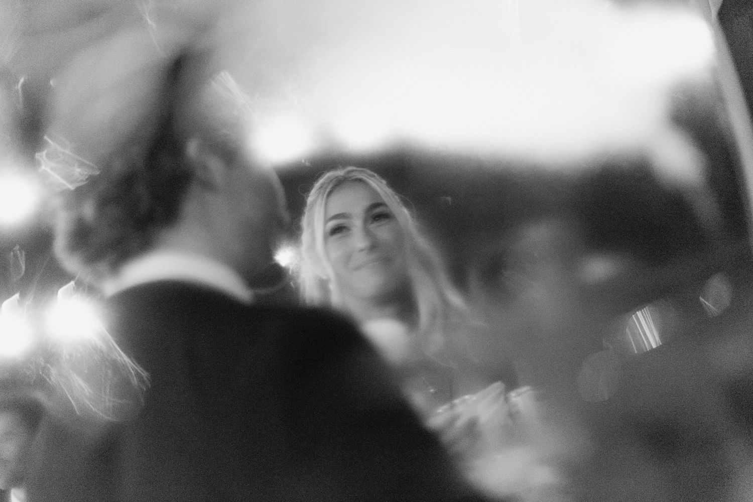 Dreamy black and white bokeh photo of smiling blonde bride at wedding reception dinner.