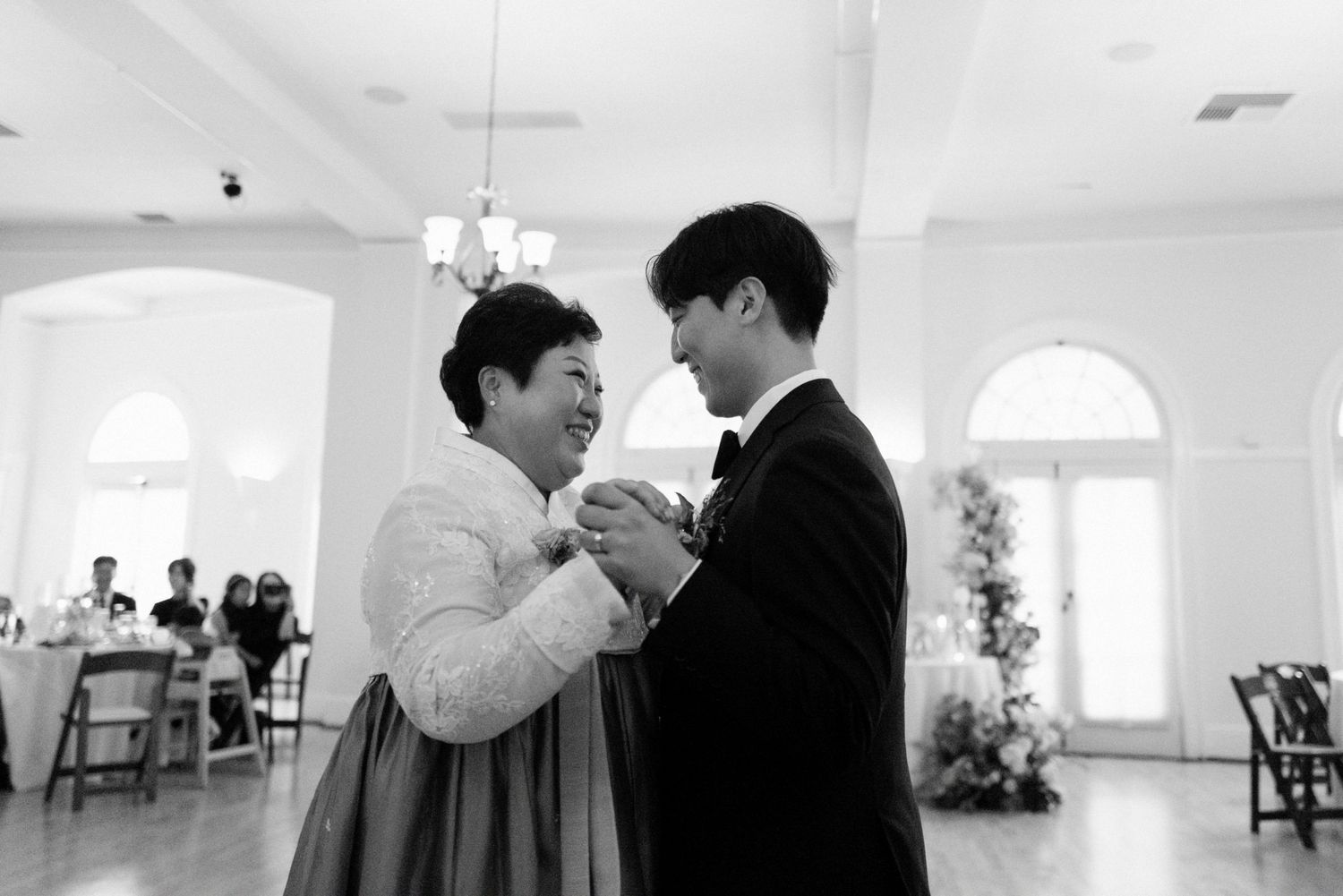 Black and white photo of groom dancing with mother in traditional hanbok.