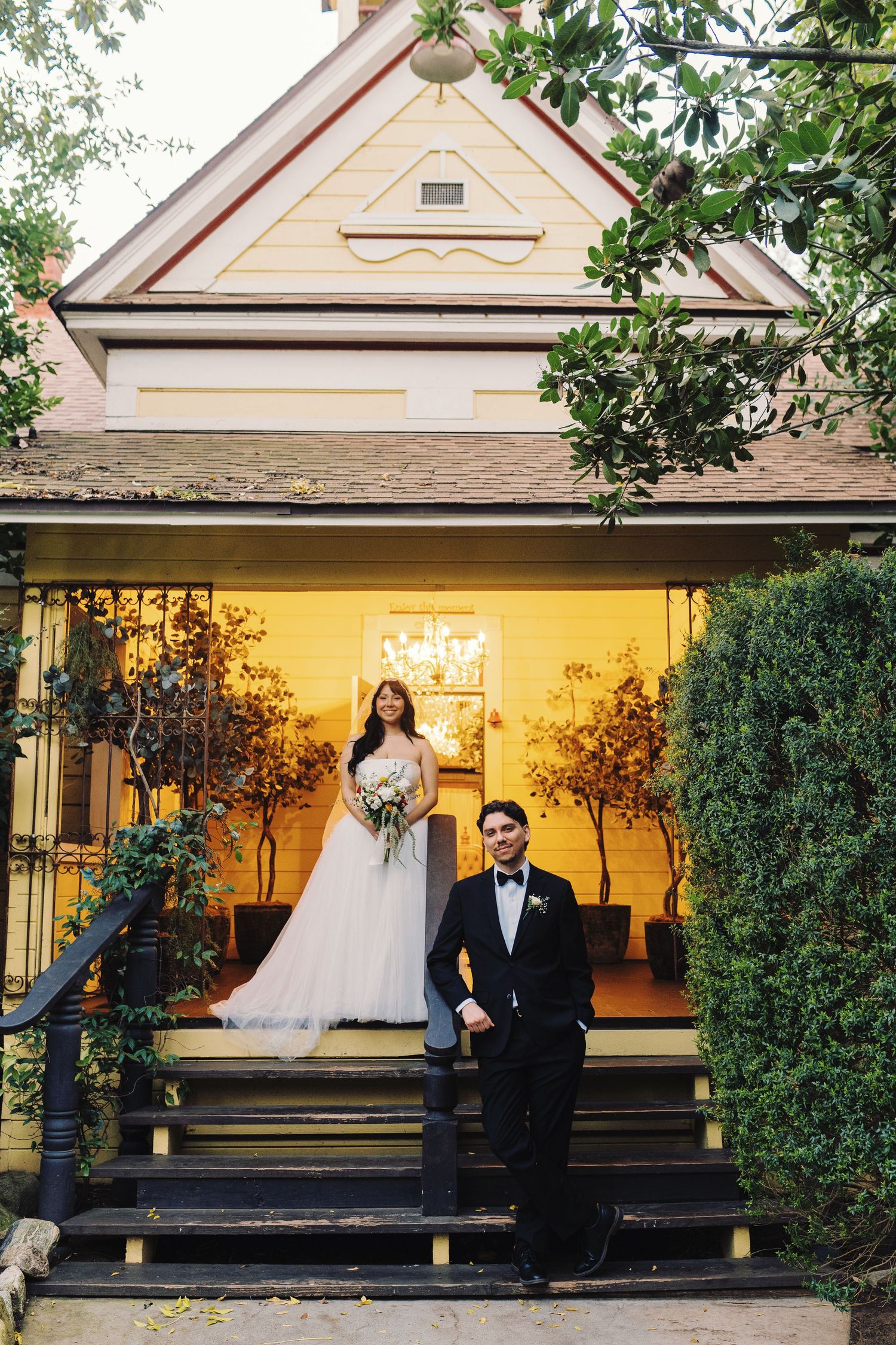 Elegant bride and groom pose on steps of a charming Victorian wedding venue at dusk.