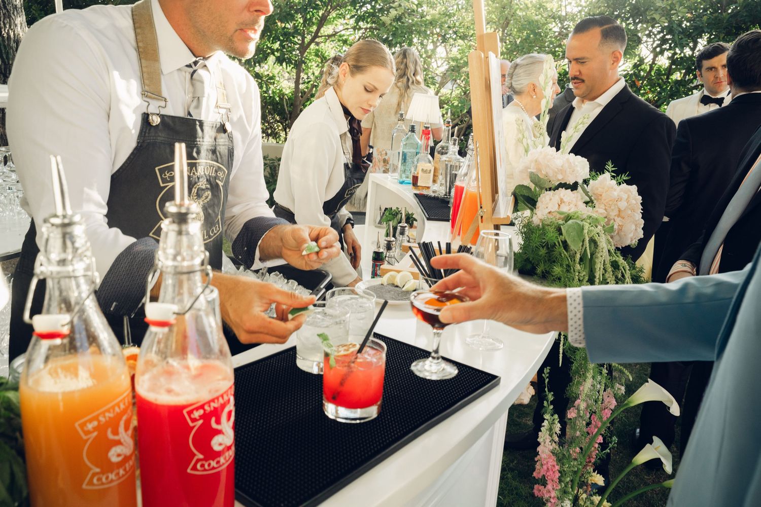 Wedding bartenders serve colorful cocktails at an elegant outdoor open bar reception.
