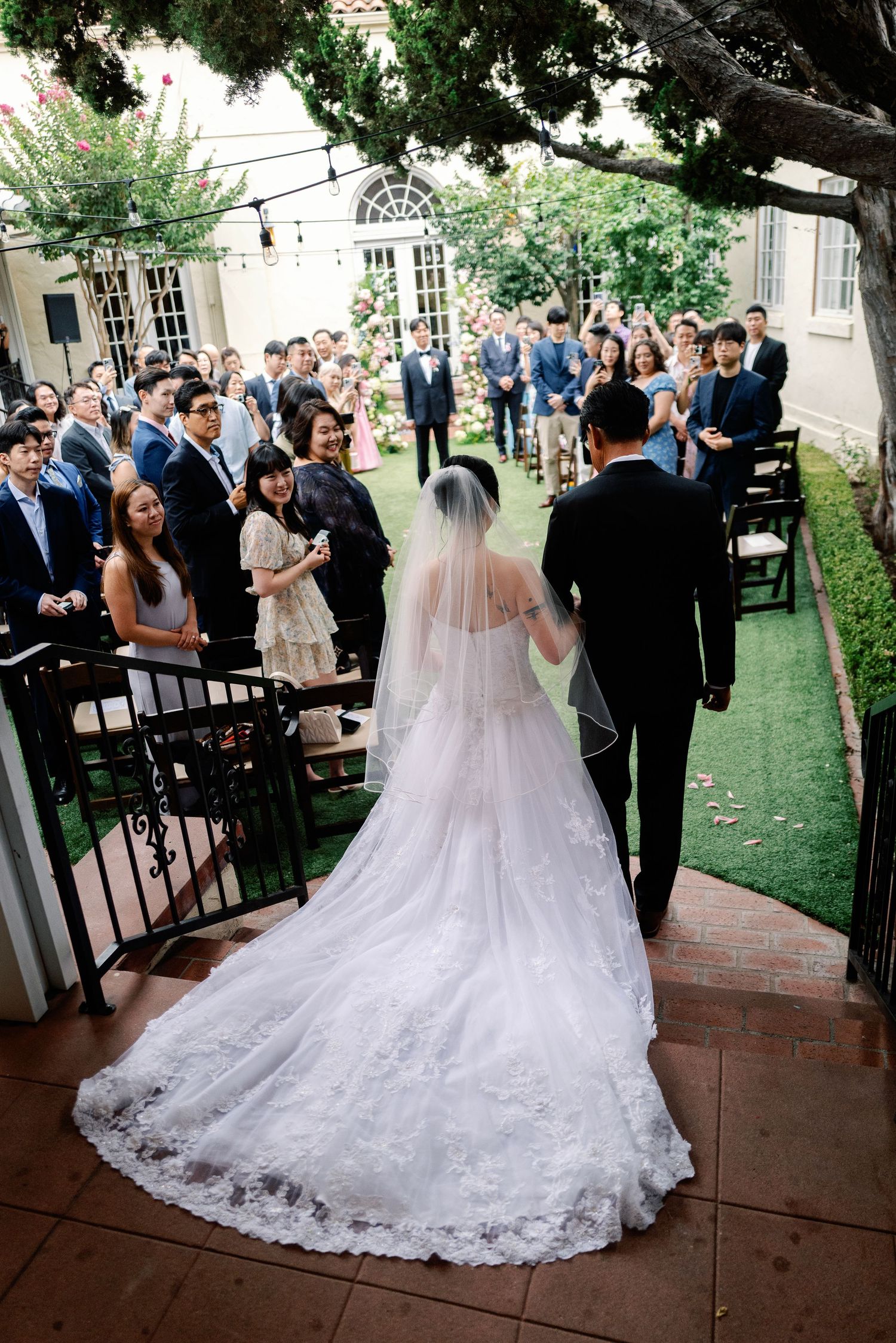 Bride in a lace gown with long veil walks down the aisle escorted by her father.