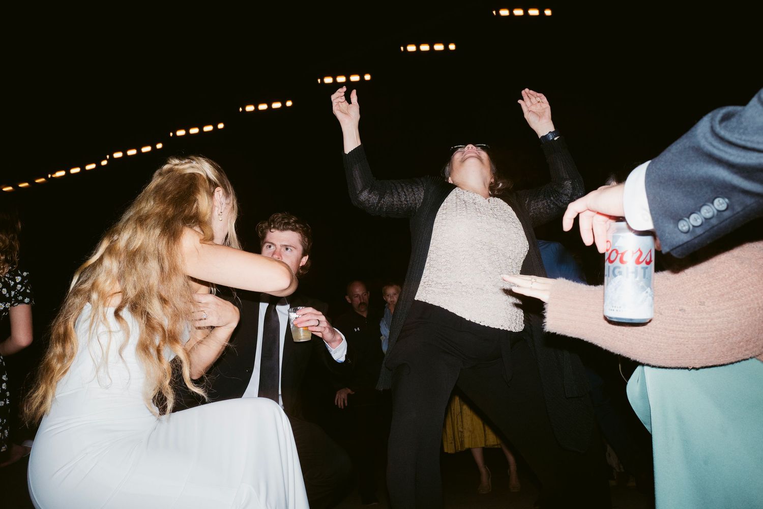Energetic wedding guests dancing wildly under string lights at outdoor evening reception.
