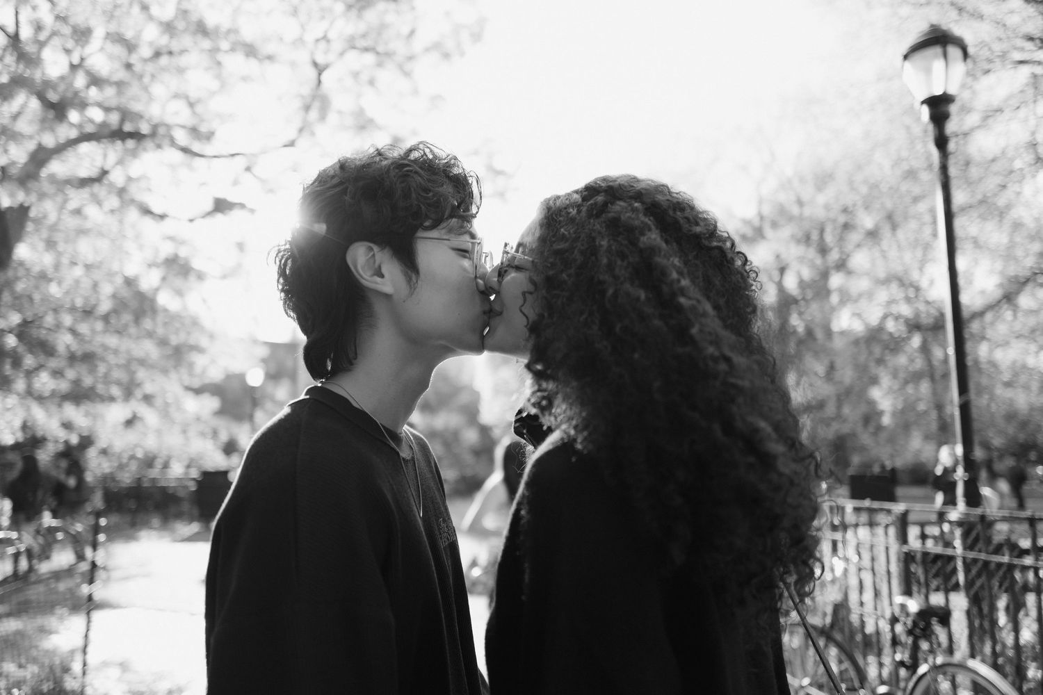Romantic black and white photo of a couple sharing a kiss outdoors in a park setting.