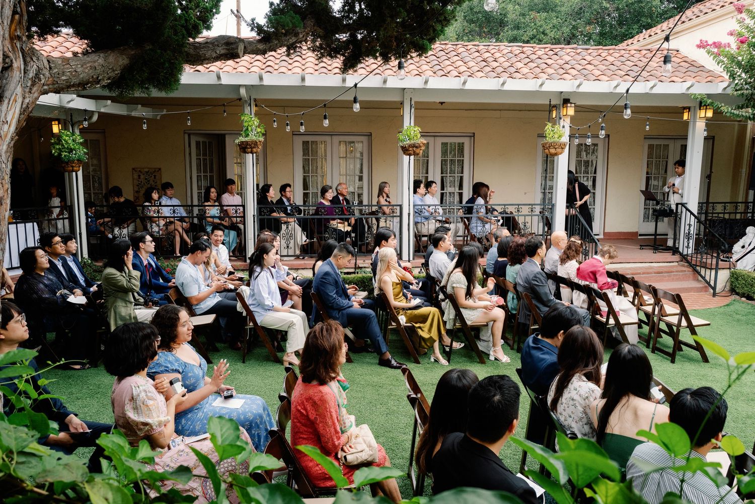 Guests seated outdoors at an elegant garden wedding ceremony at a Spanish-style villa.