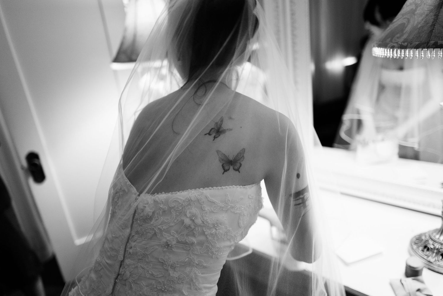 Black and white photo of bride in lace gown with butterfly tattoos on her back.