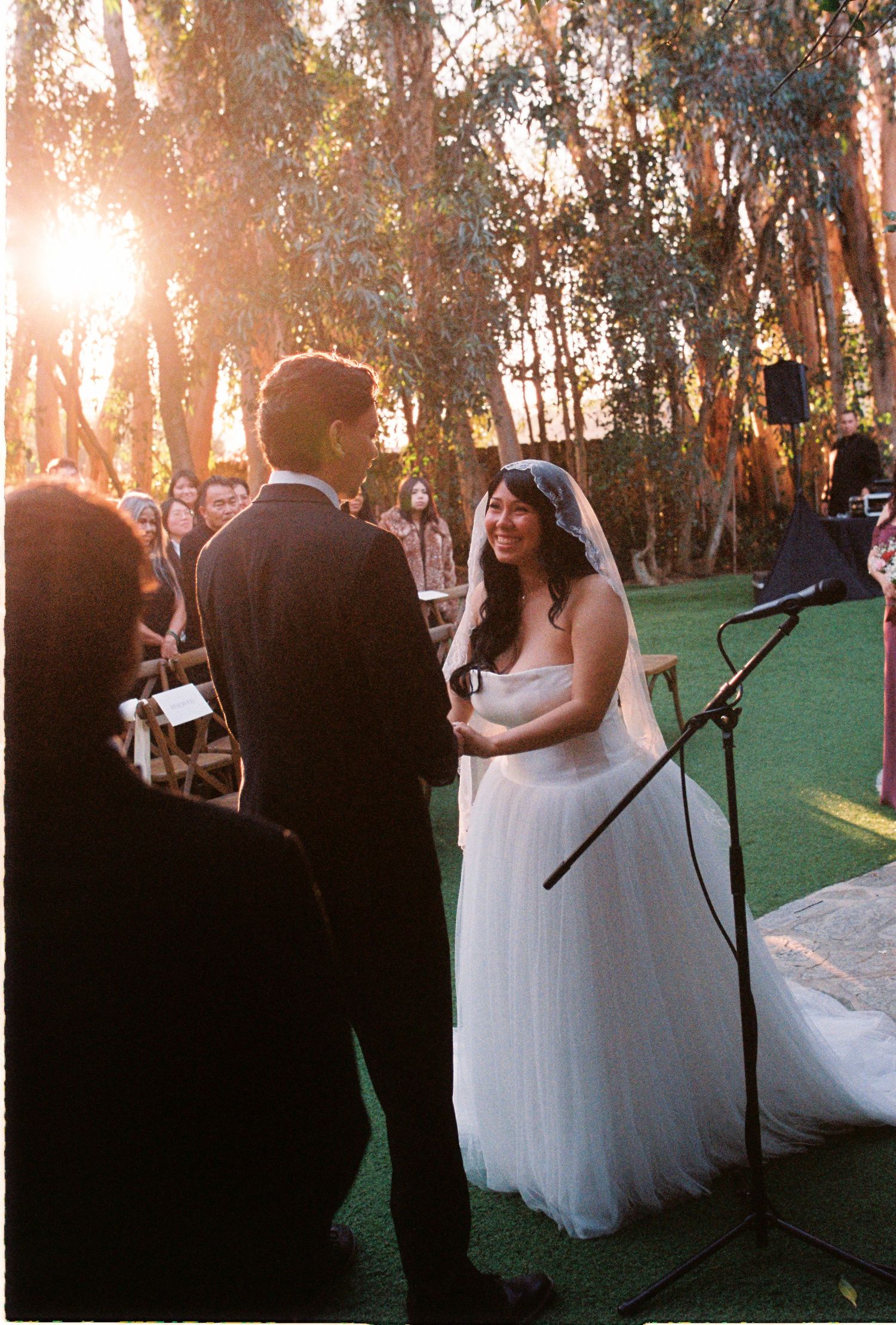 Bride and groom exchange vows at outdoor garden wedding ceremony bathed in warm golden sunset light.