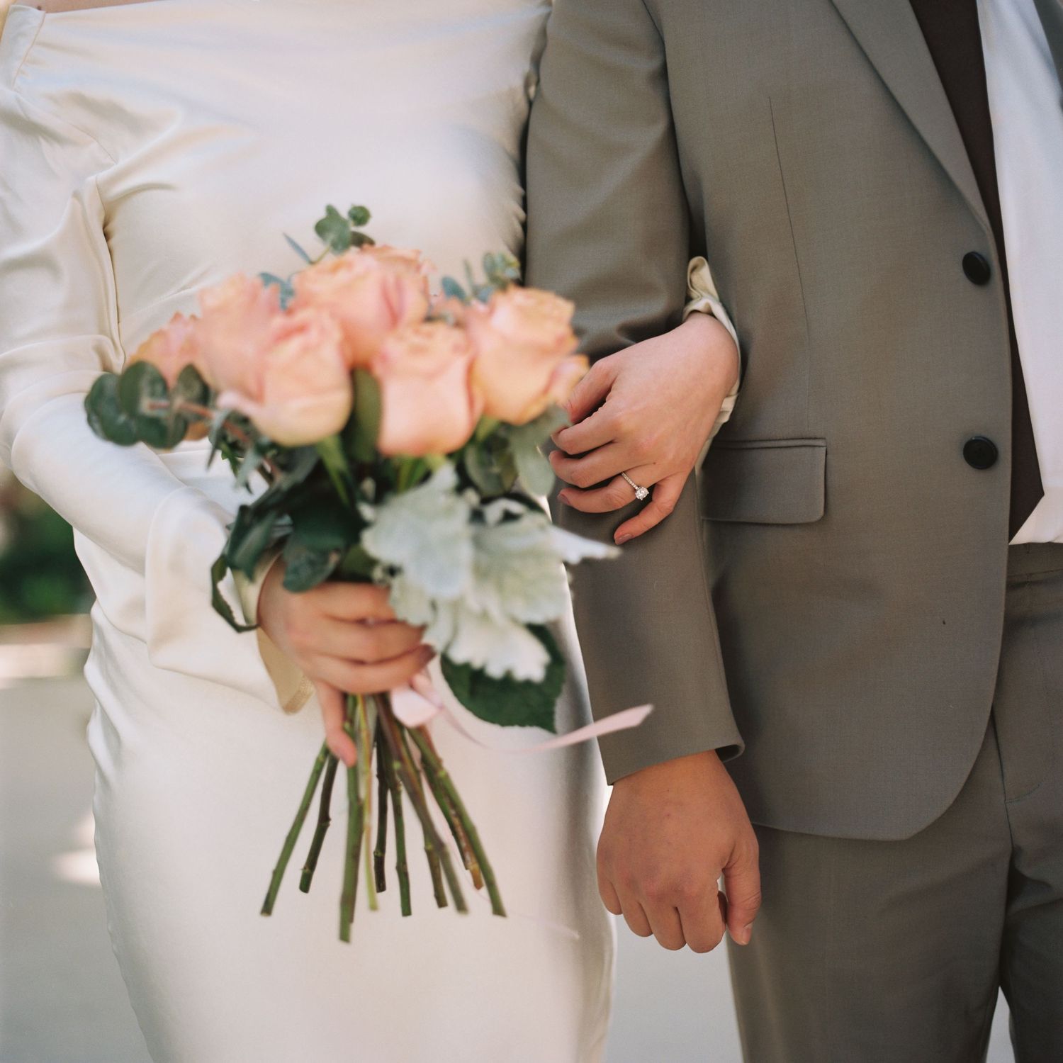 Bride and groom holding hands with a beautiful pink rose and white flower wedding bouquet at their ceremony.