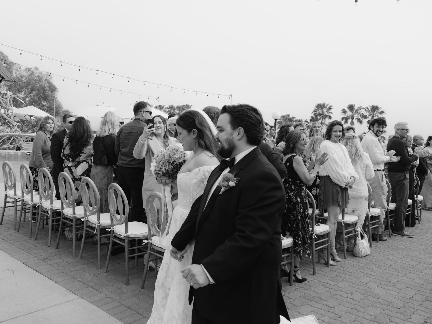 Black and white photo of bride and groom walking up aisle after wedding ceremony.