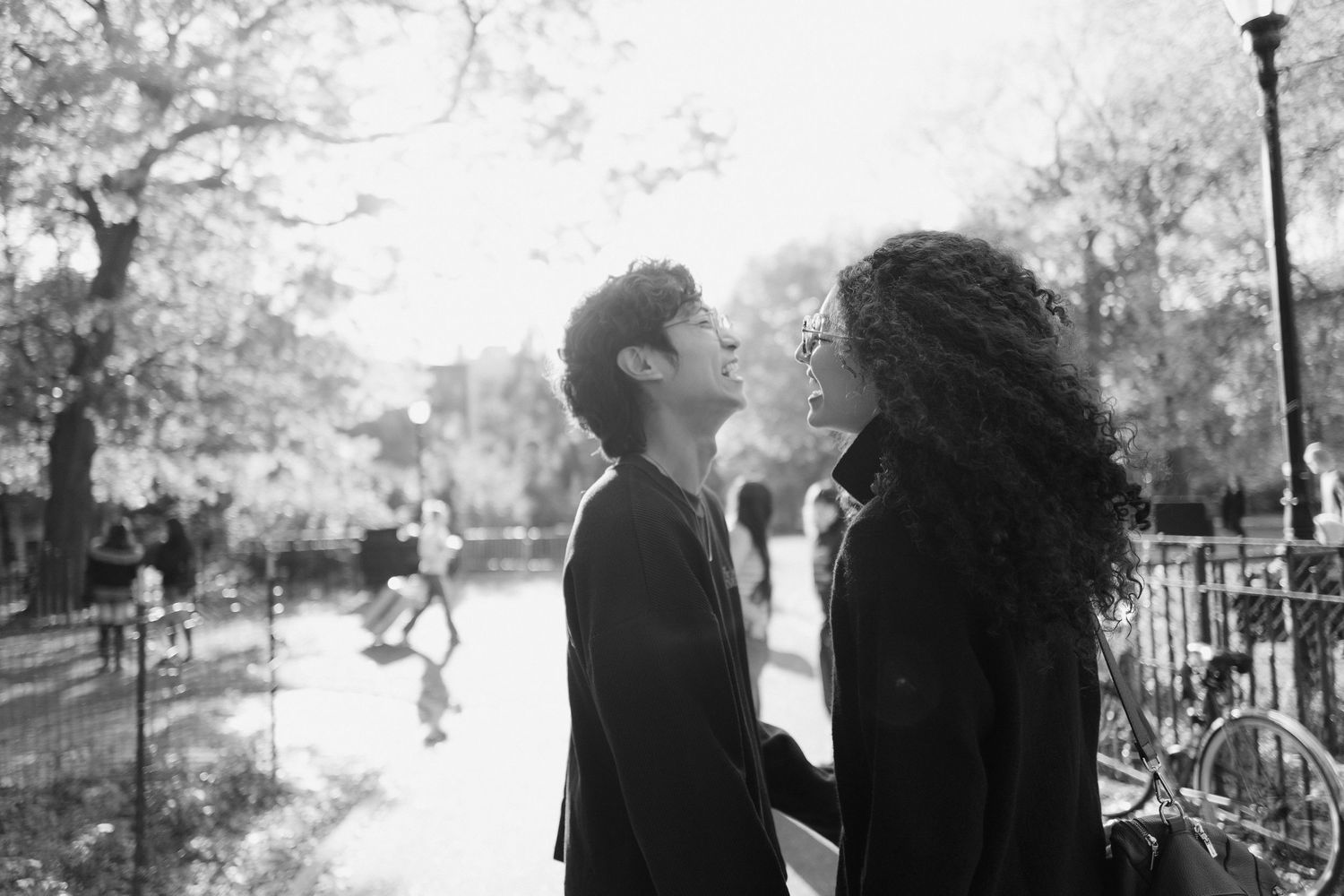 Couple standing close together in a sunlit park, gazing at each other romantically in black and white.