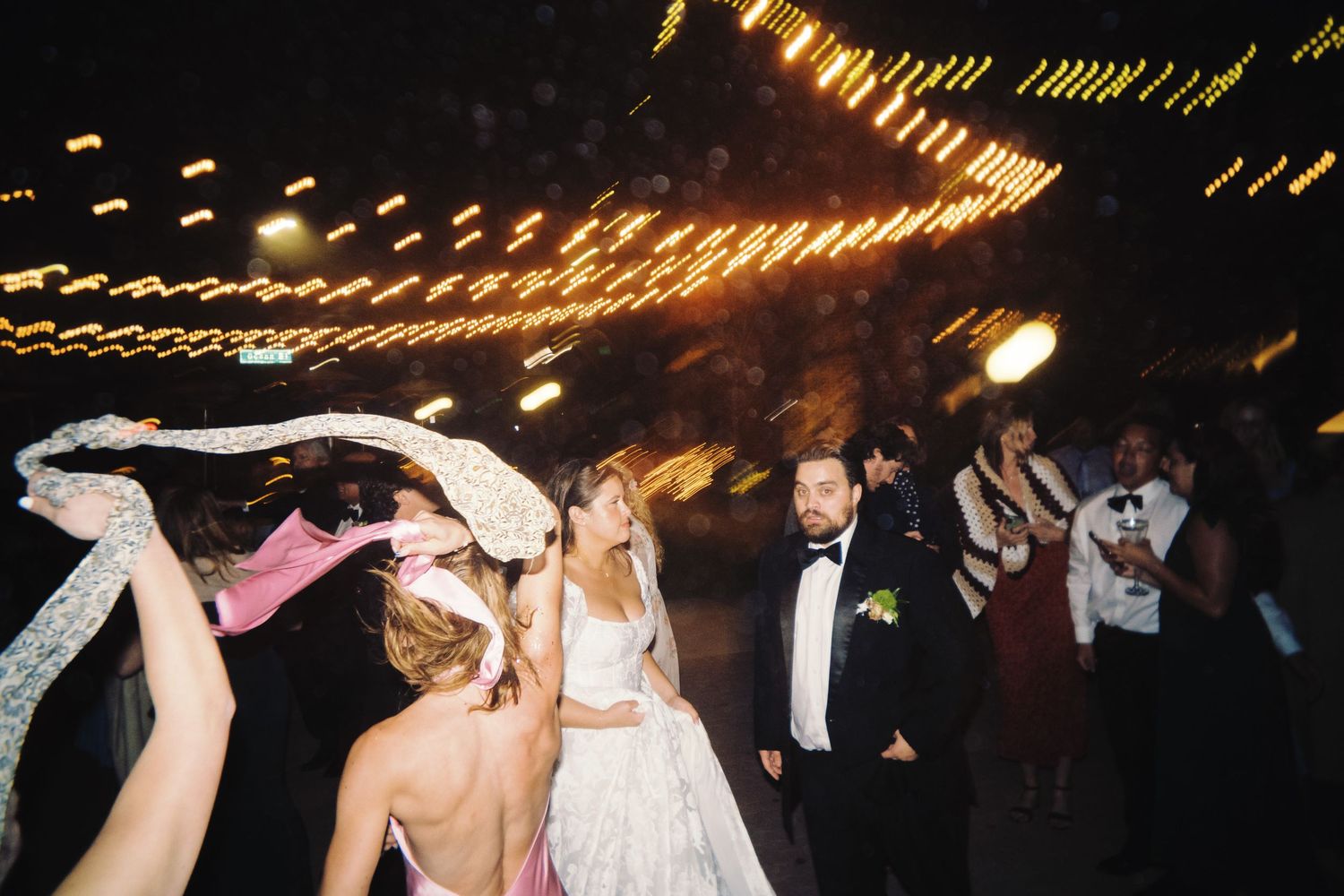 Bride and groom dancing joyfully with guests at a lively outdoor nighttime wedding reception.