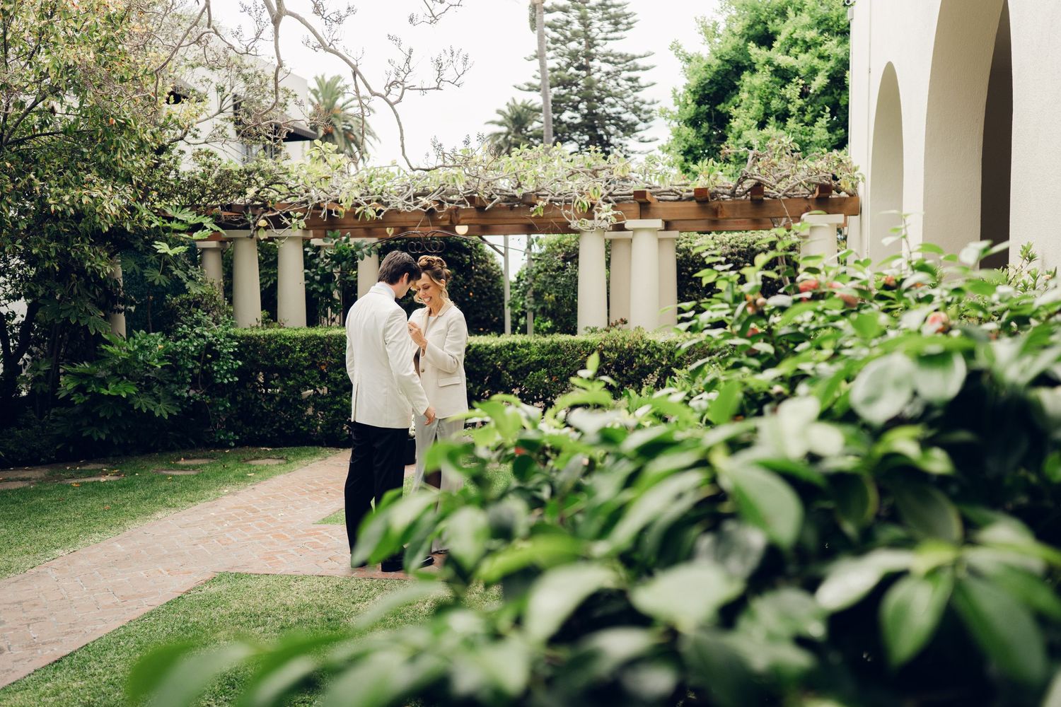 Bride and groom share a romantic moment in a lush garden with a flower-covered pergola.