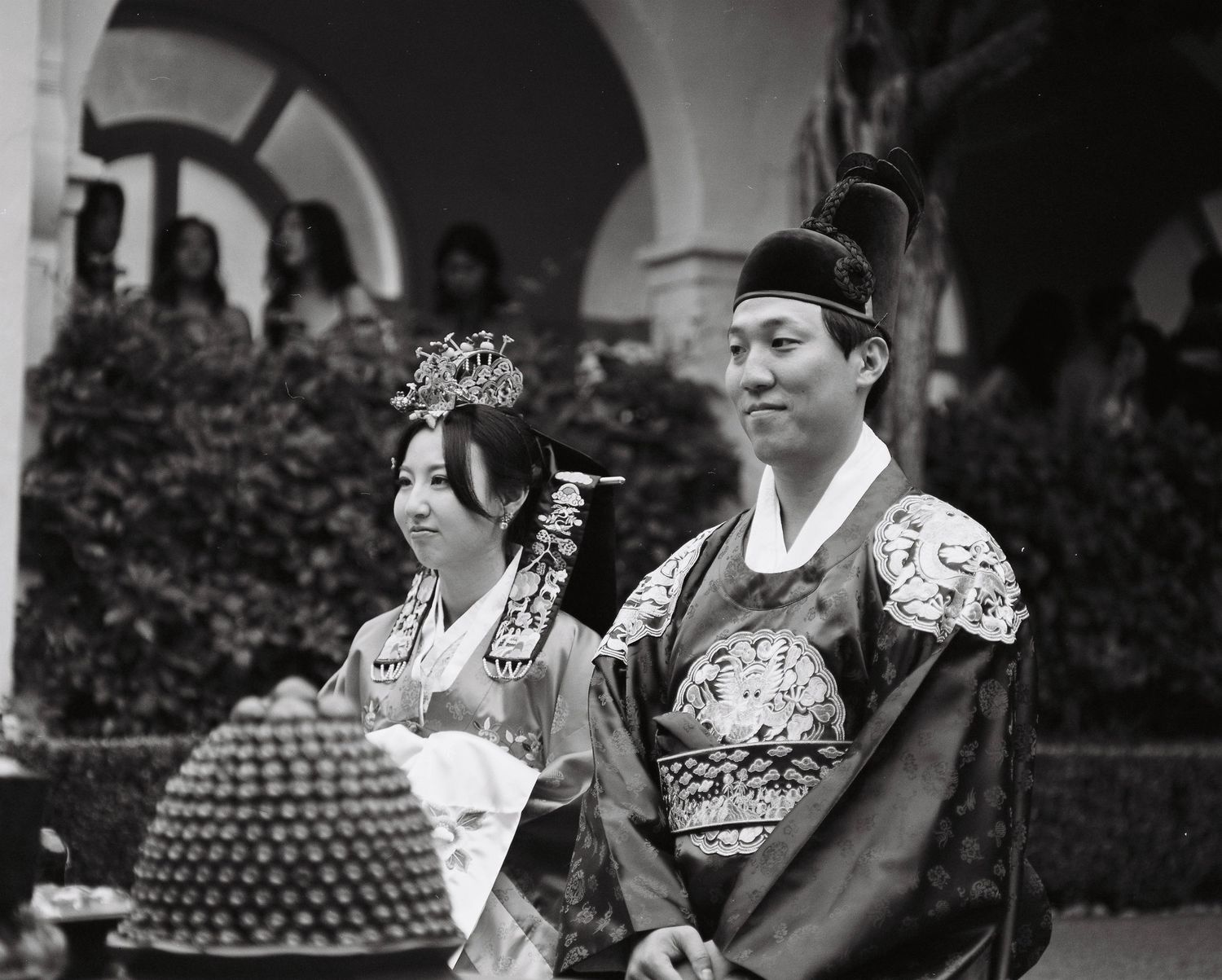 Bride and groom in ornate traditional Korean wedding hanbok during outdoor ceremony.