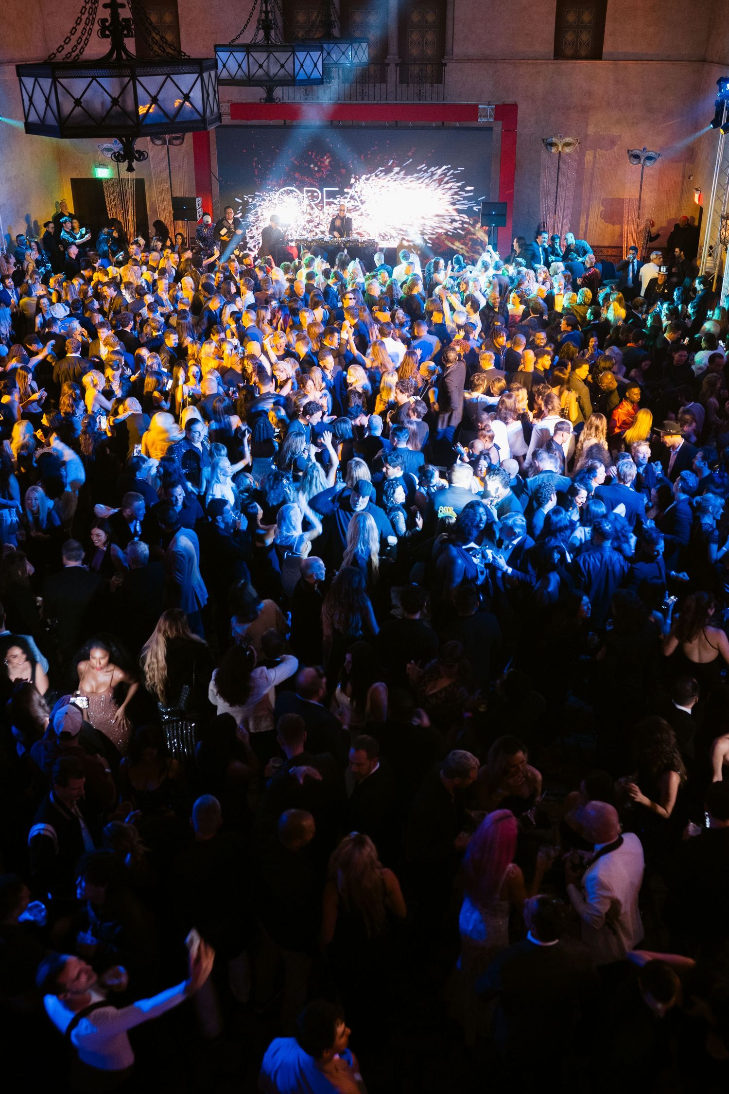 Large crowd of people dancing at a nightclub event with blue lighting and sparkling stage backdrop.