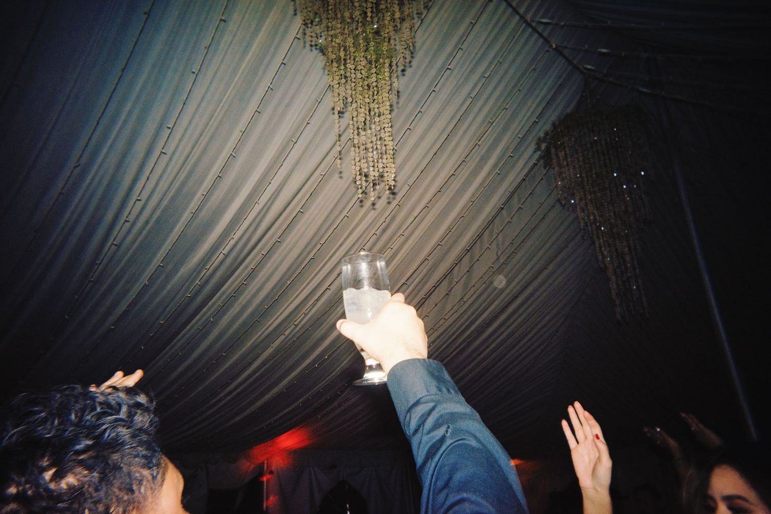 Wedding guest raises champagne glass in toast under draped ceiling at festive reception.