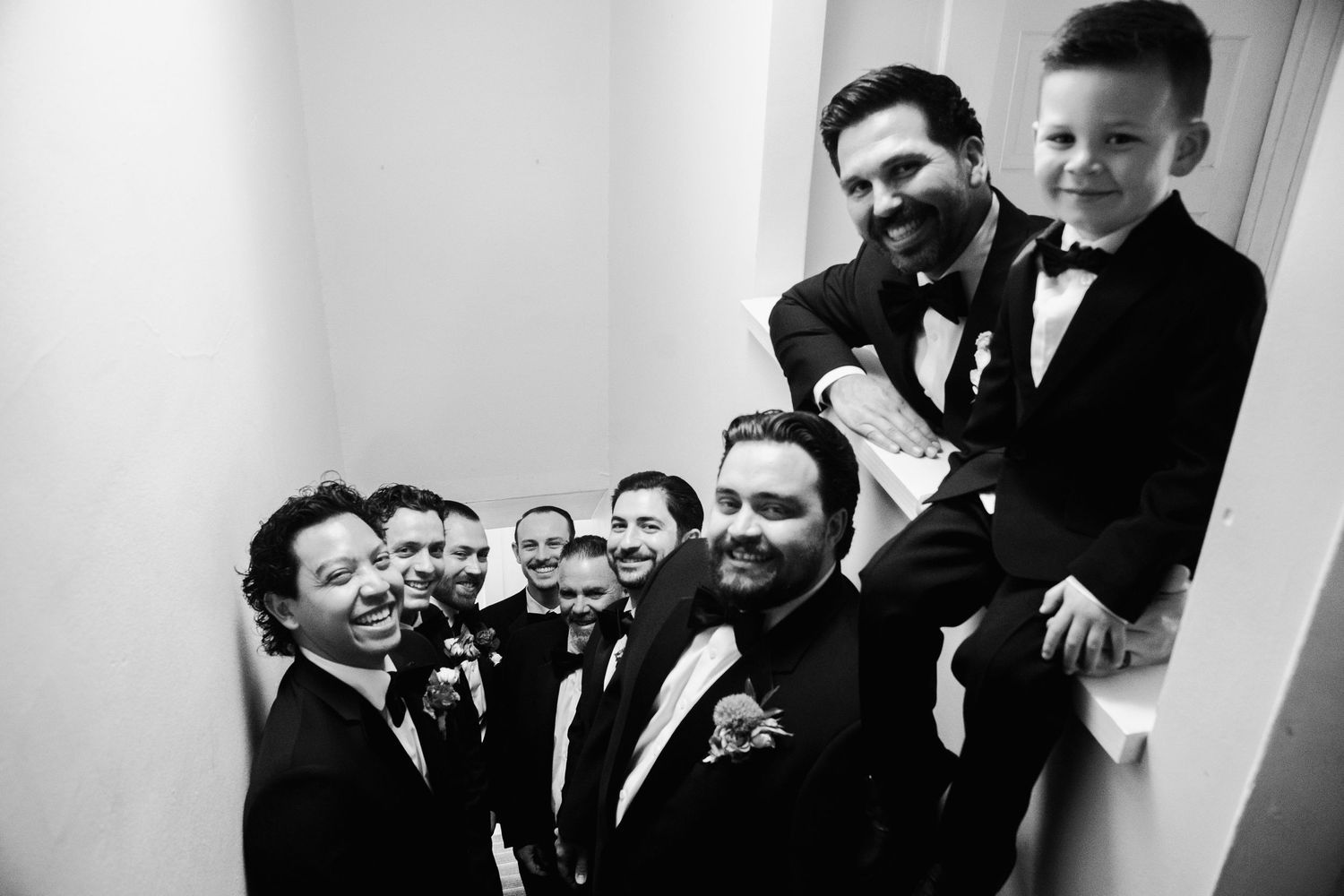 Black and white photo of groom with groomsmen and young boy smiling in stairwell.