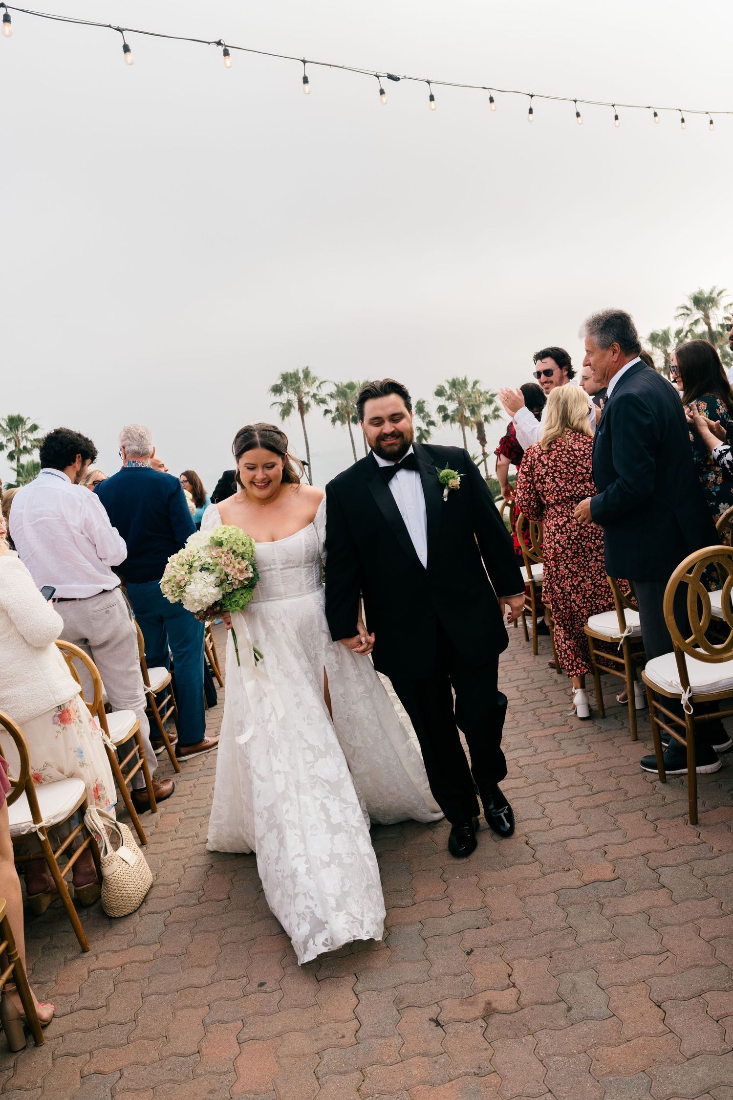 Newlyweds walk back down aisle hand in hand after outdoor wedding ceremony.