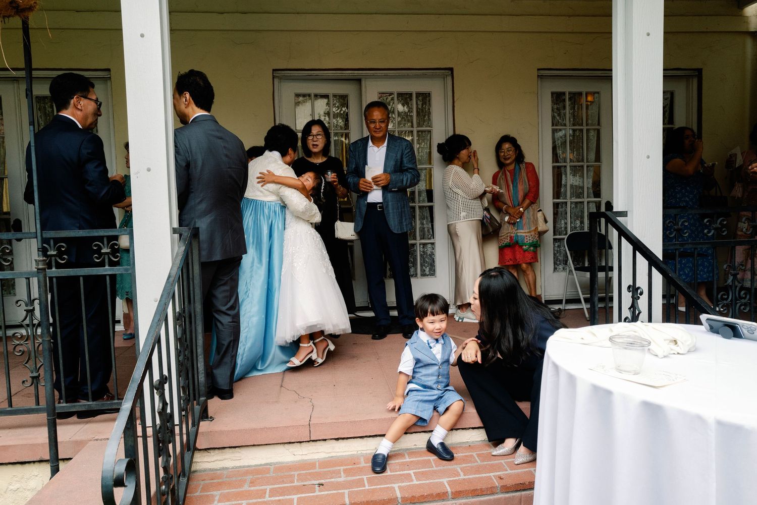 Wedding guests gather on venue steps as young child sits on stairs at outdoor reception.