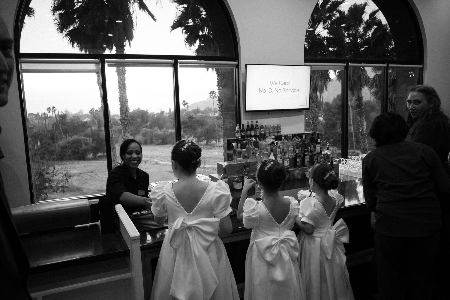Black and white photo of flower girls in white dresses with bows at a wedding ceremony inside a church.
