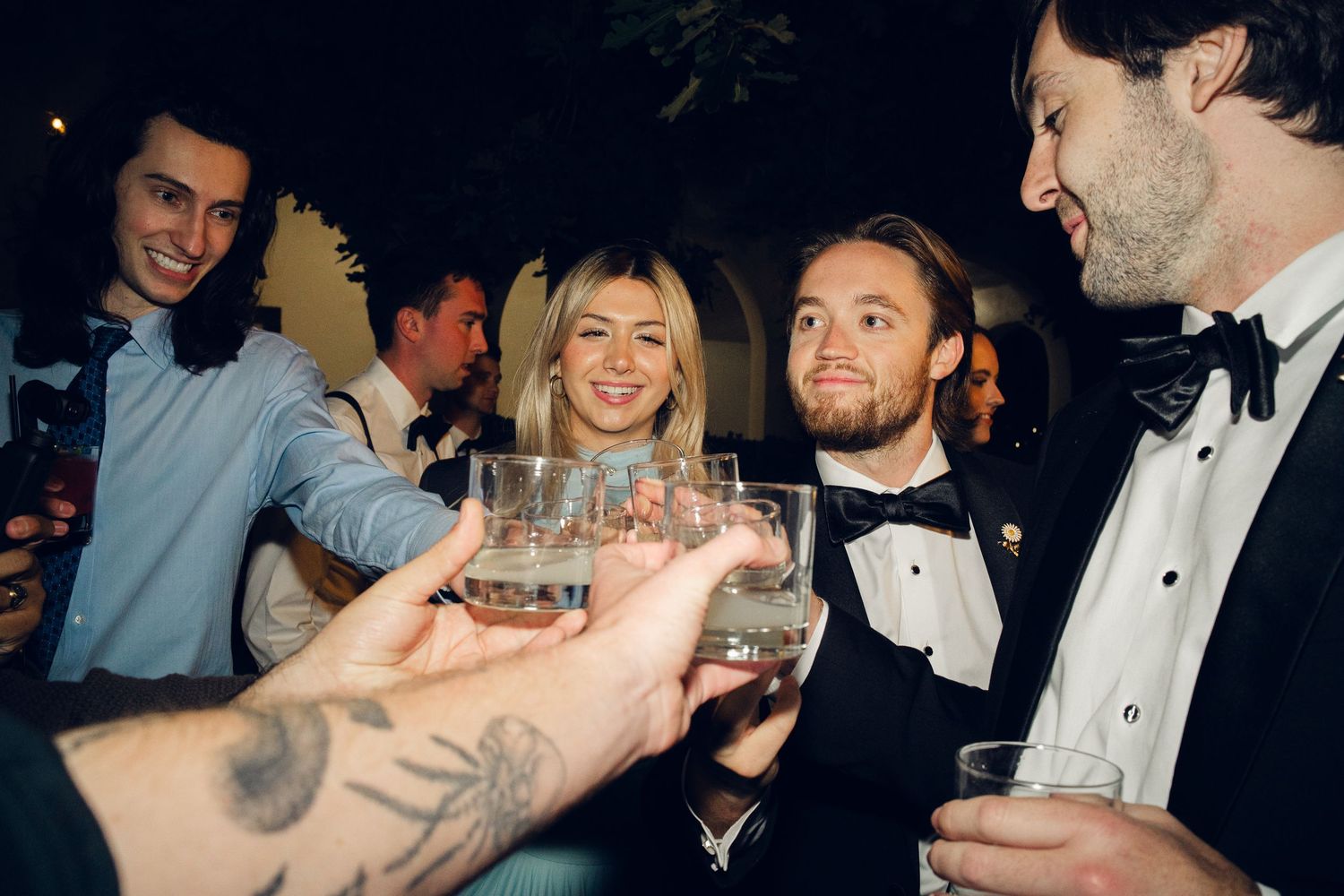 Guests in formal attire clink glasses in a celebratory toast at a nighttime wedding reception.