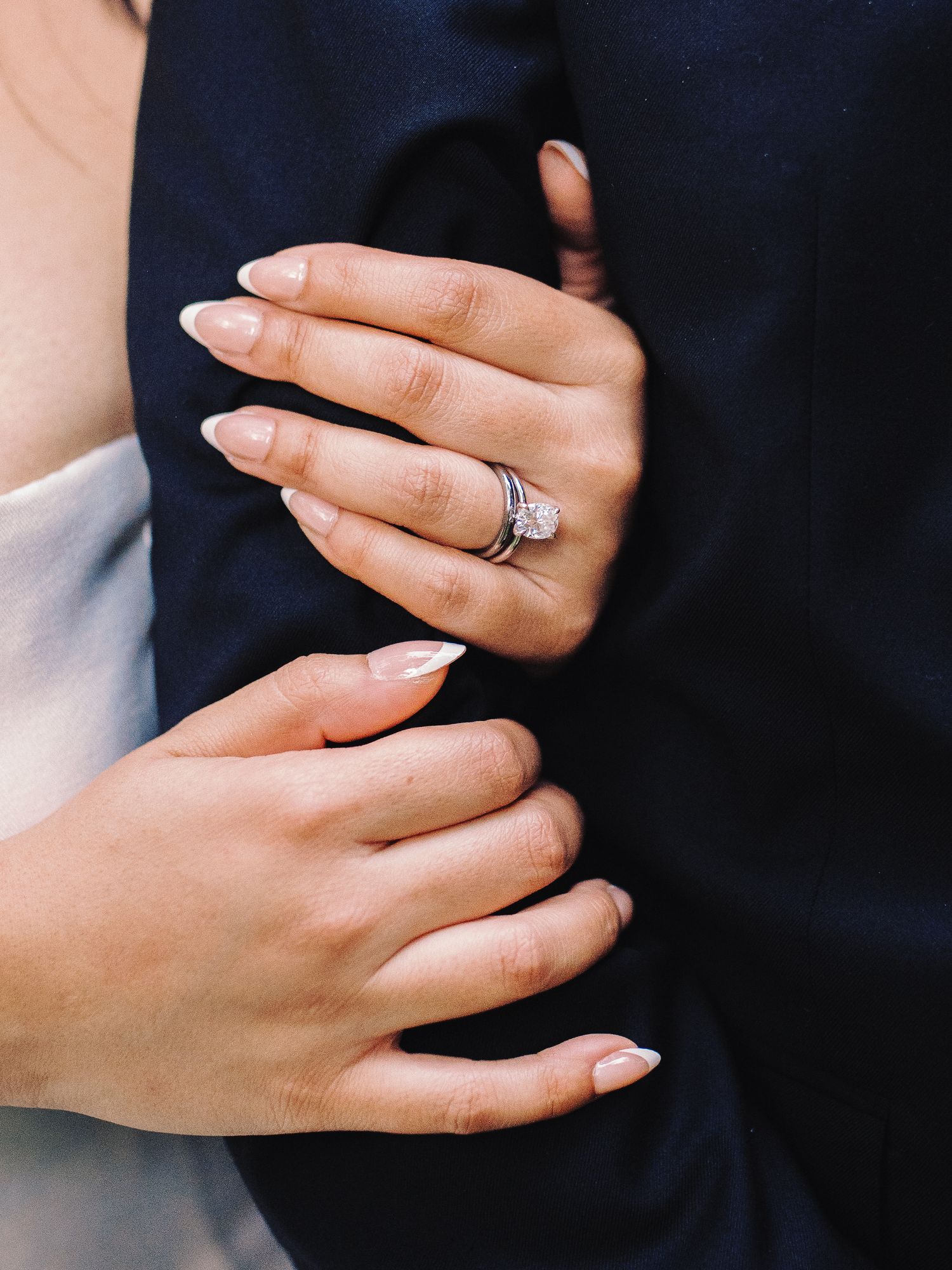Close-up of bride's diamond engagement ring and wedding band as she holds groom's arm.